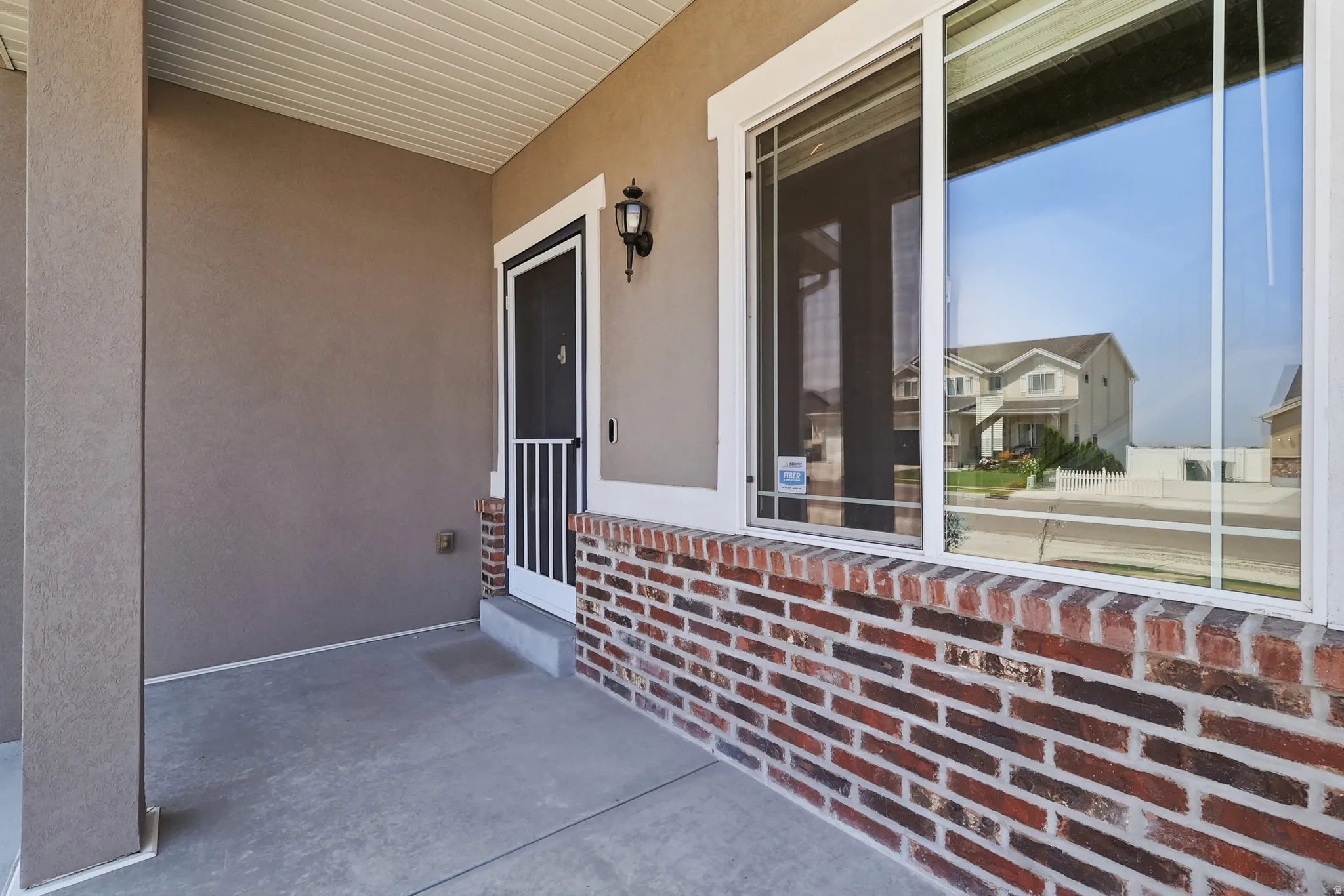 Covered entryway featuring a concrete patio, brick wainscoting, stucco siding, and a screen door with an exterior light fixture