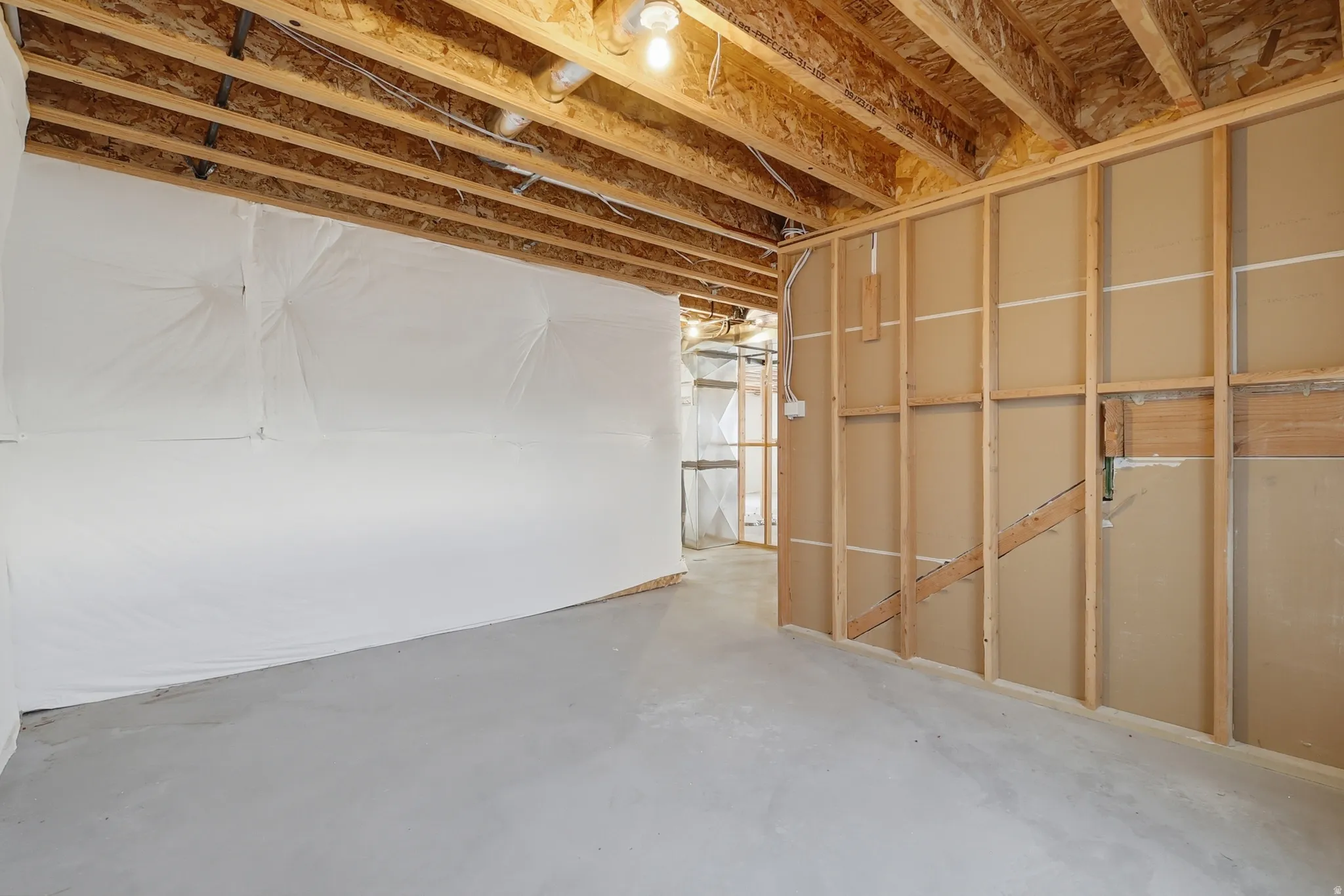 Unfinished basement space featuring exposed wood joists and subflooring, concrete flooring, and partial wall framing