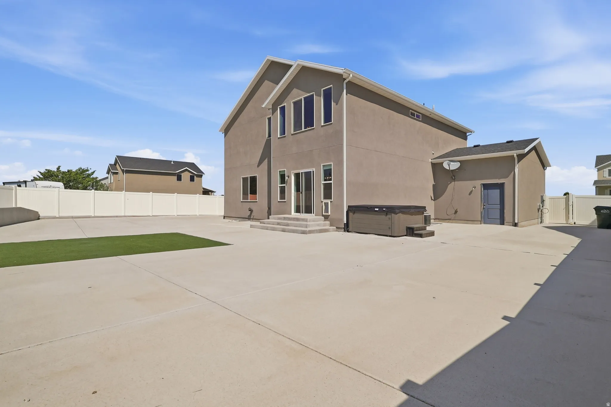 Expansive concrete patio area featuring a built-in spa, a section of artificial turf, and a vinyl privacy fence
