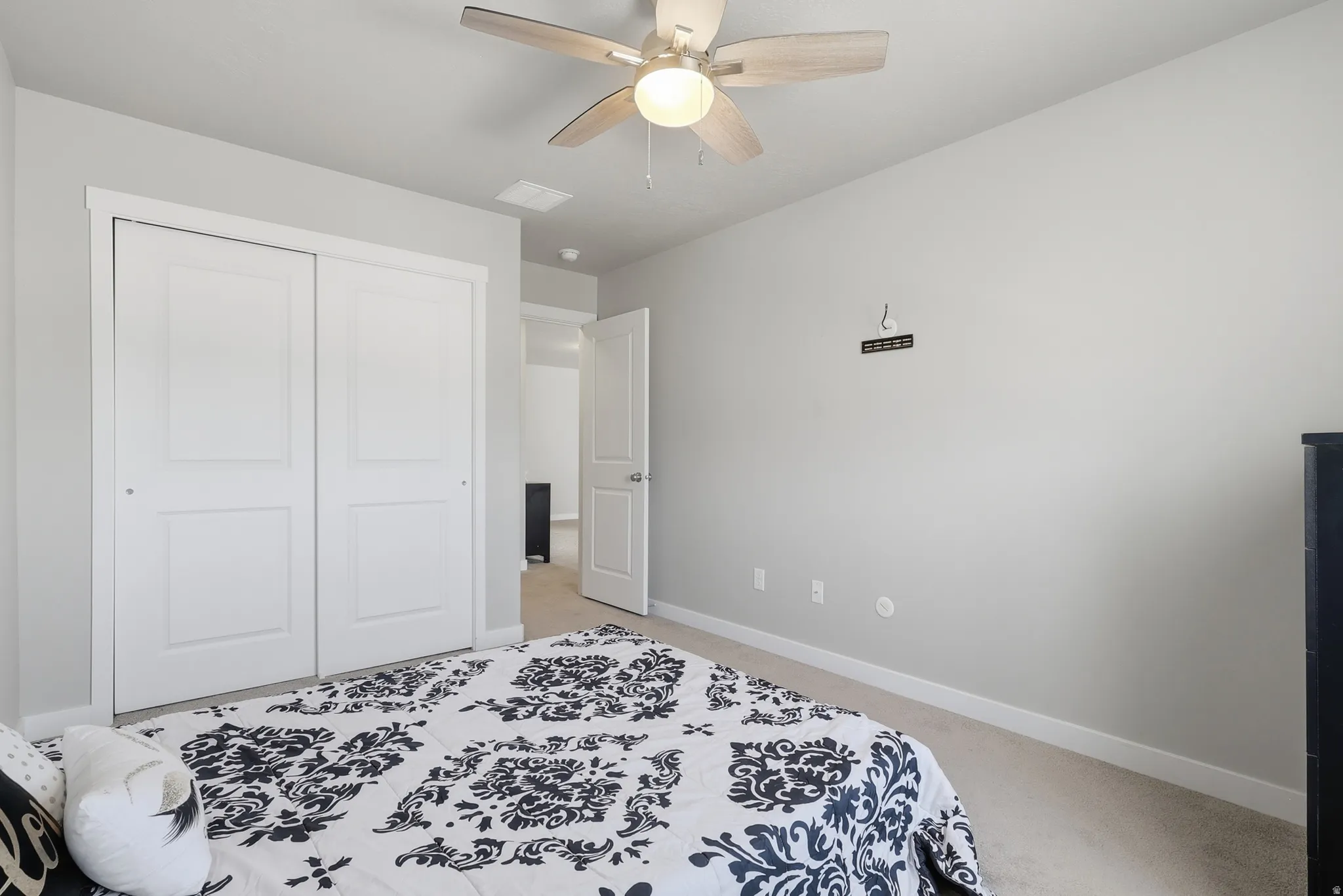 Bright interior space with light gray walls, plush carpeting, a white bi-fold closet, a ceiling fan with integrated lighting, and white trim throughout