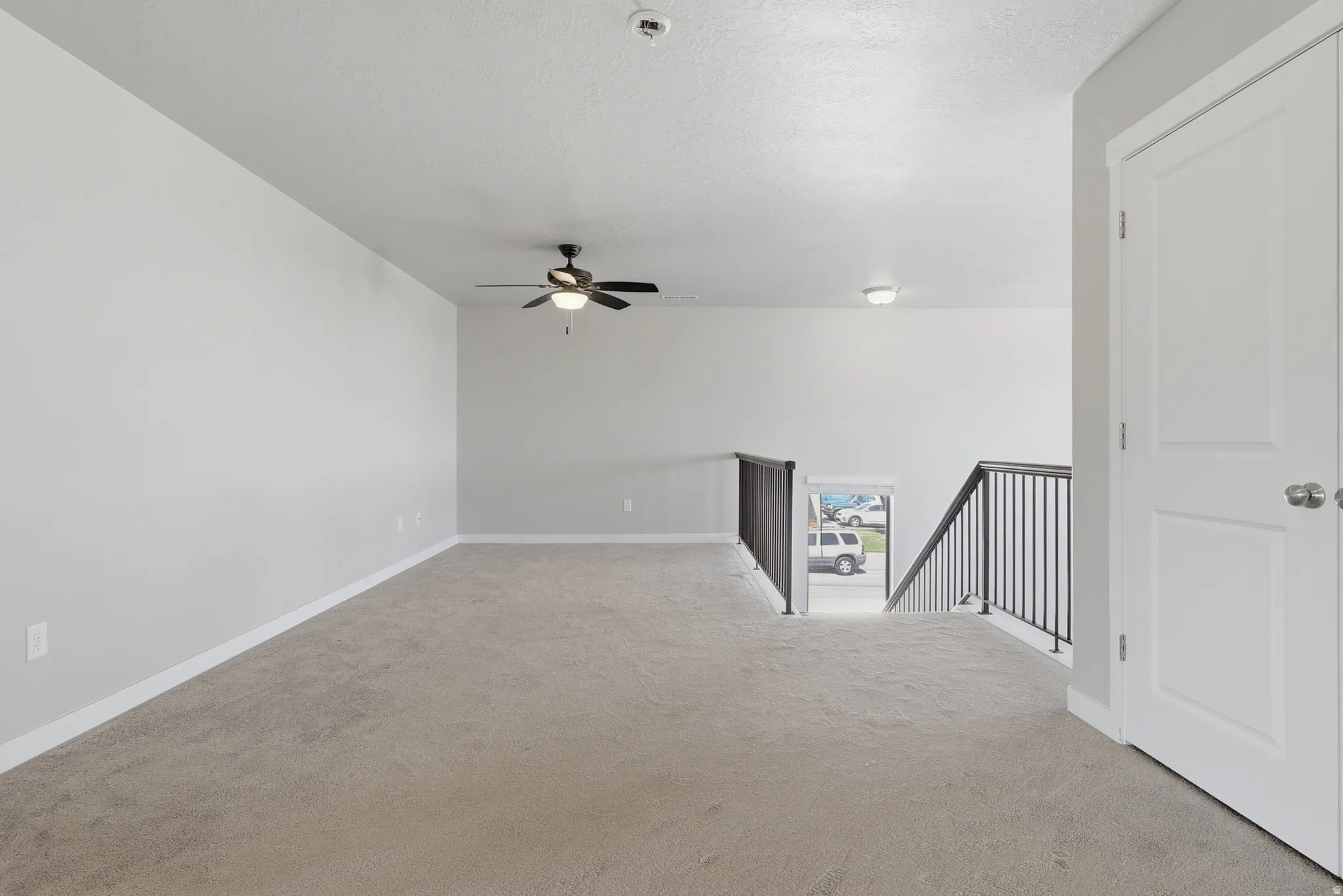 Spacious carpeted upper-level area featuring a ceiling fan, recessed lighting, and a white paneled door