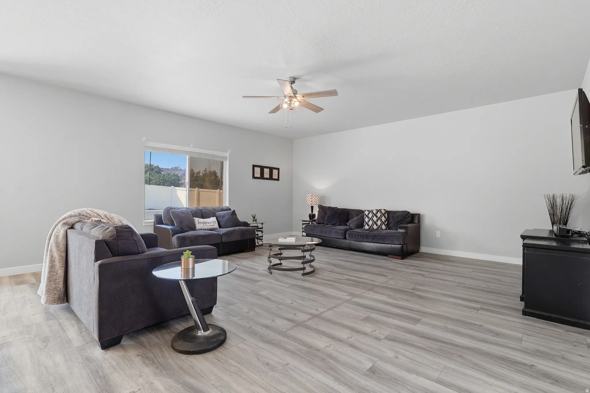 Spacious room featuring wood-finish flooring, a contemporary ceiling fan with integrated lighting, and neutral wall tones