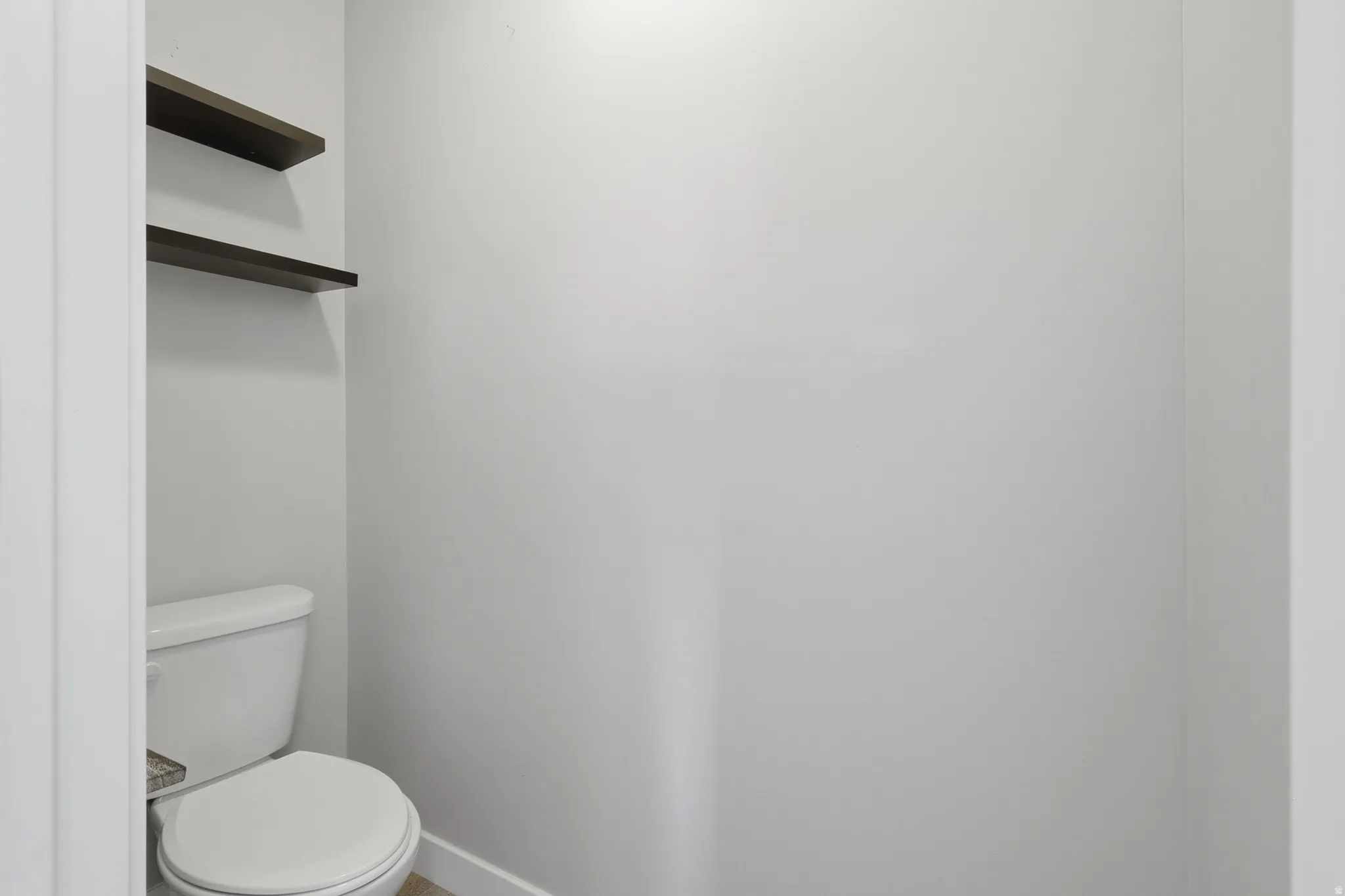 Recessed toilet area featuring a white commode and two dark-finish floating shelves
