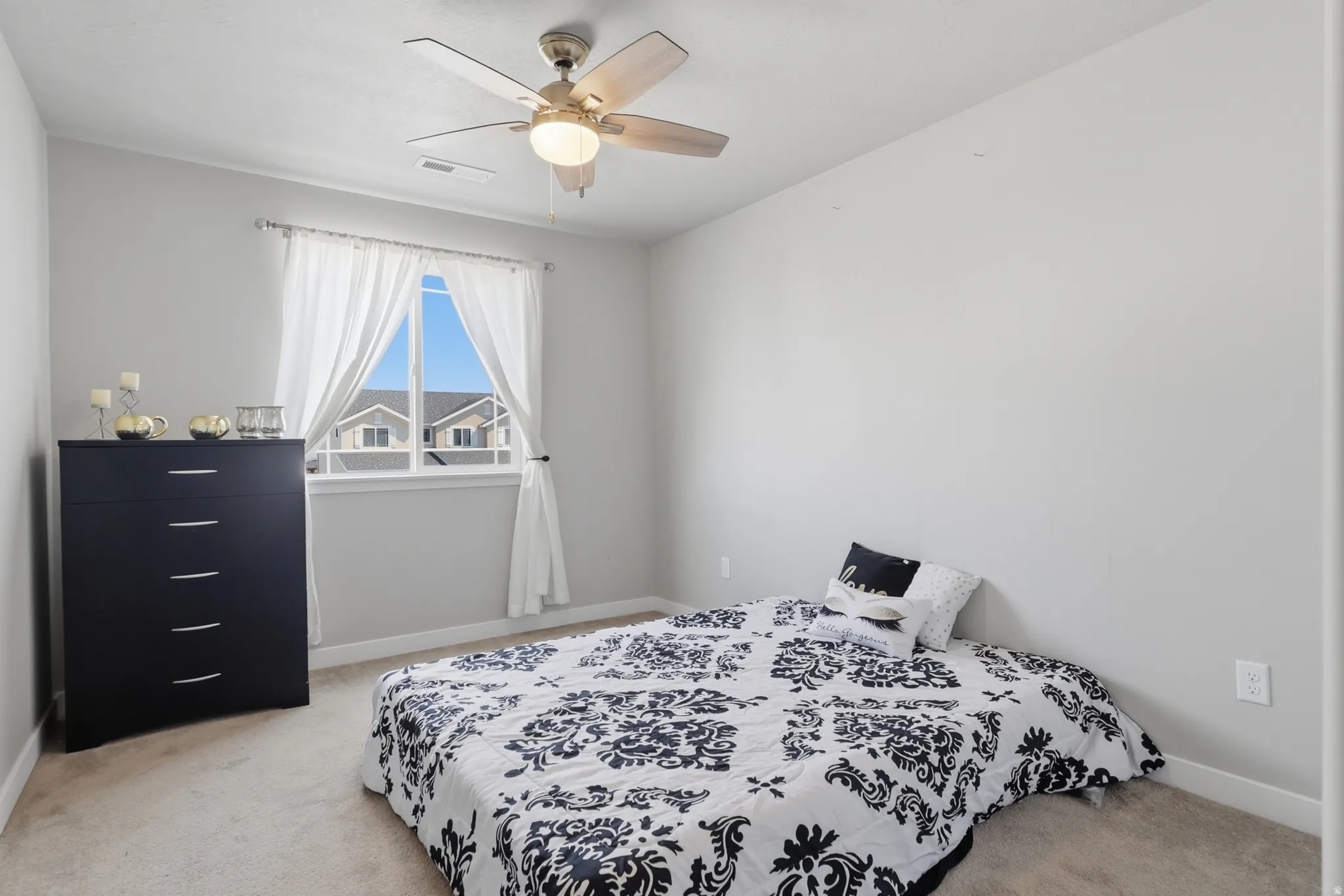 Light-filled room featuring a window with white curtains, a ceiling fan with integrated lighting, and neutral wall paint