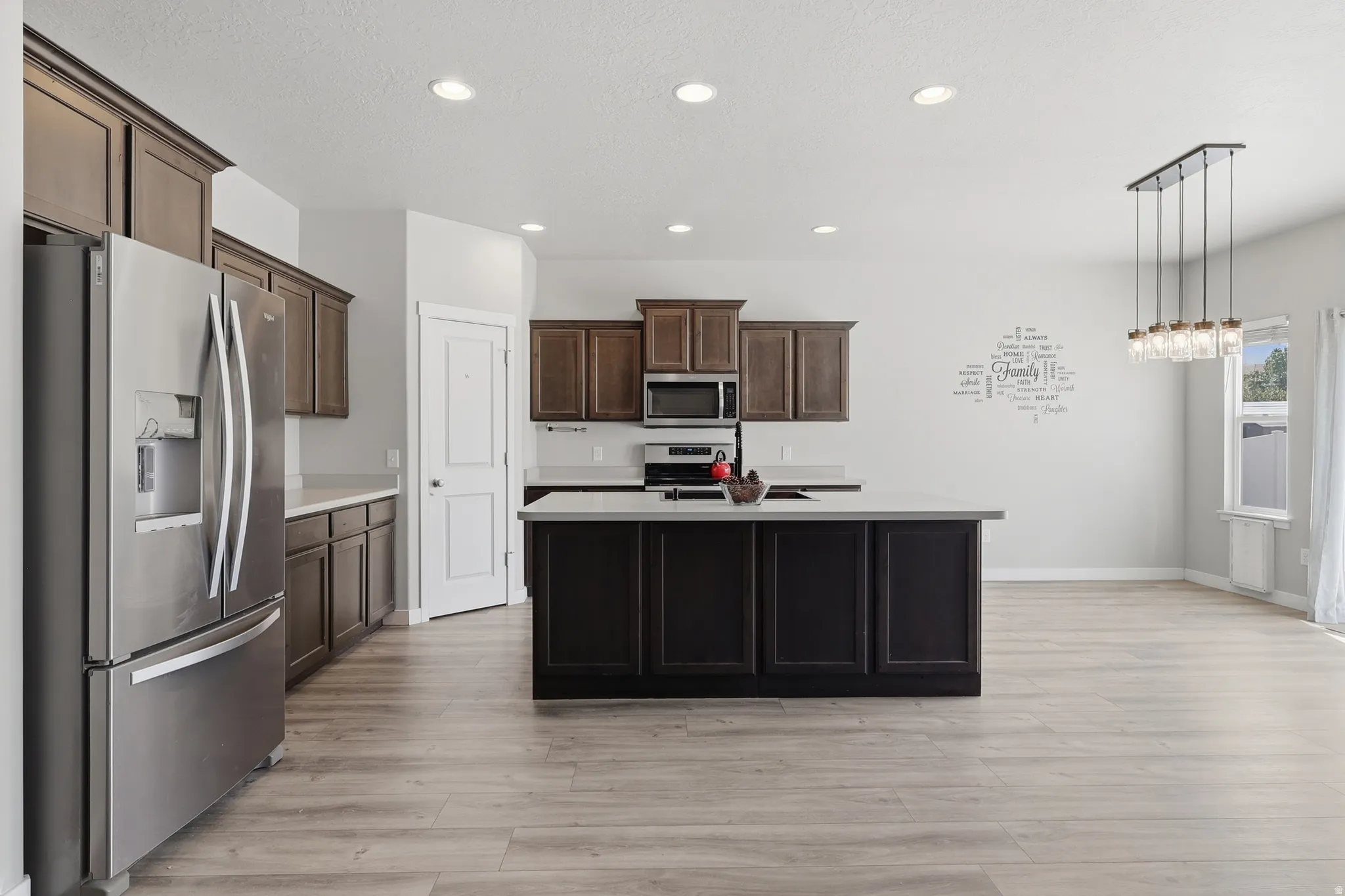 Expansive kitchen featuring stainless steel appliances, wood-finish flooring, recessed lighting, and a large central island with countertop space