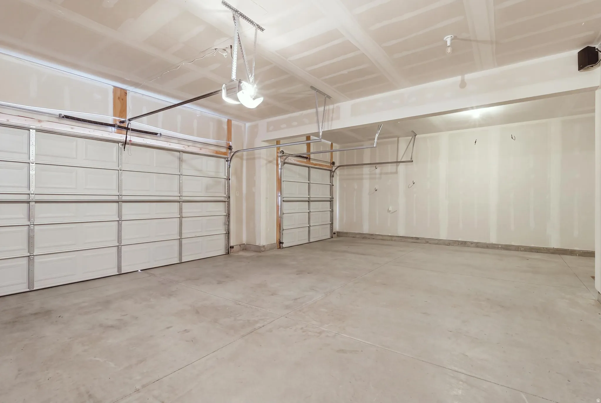 Spacious garage featuring two overhead doors, exposed drywall, concrete flooring, and an automatic door opener mechanism