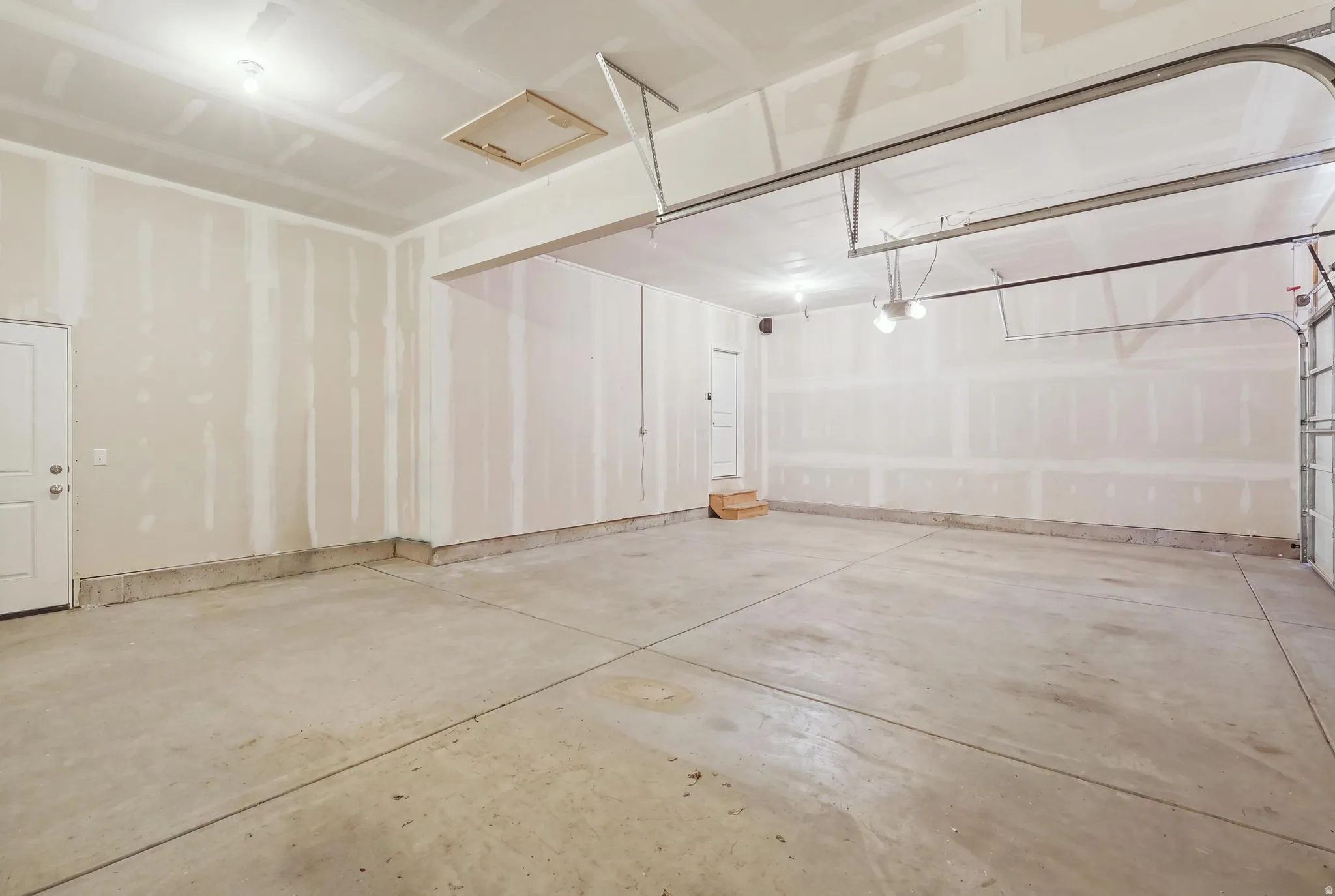 Spacious garage featuring a concrete floor, overhead lighting, and an interior access door