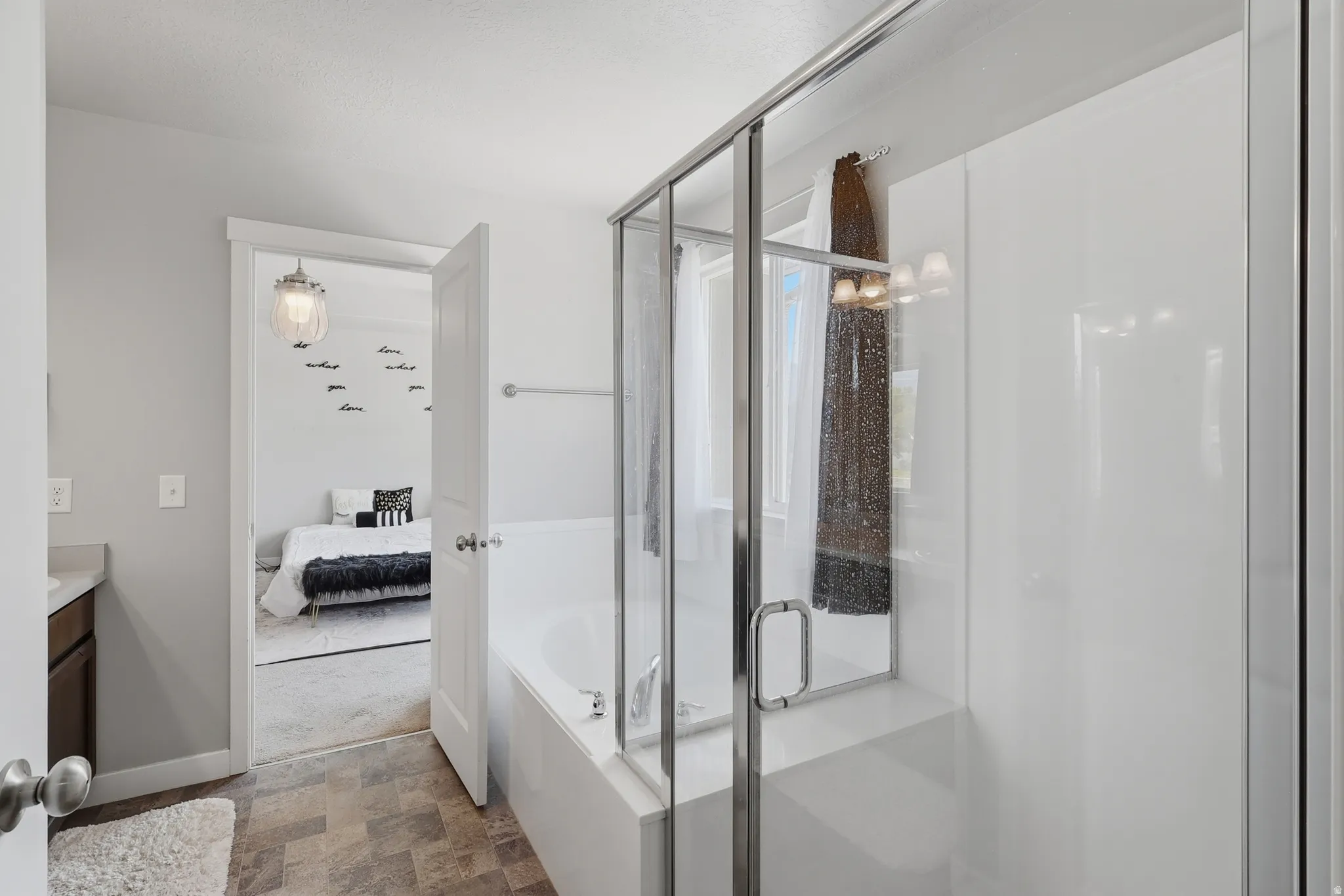 Bathroom featuring a white integrated tub and shower combination with a glass enclosure, wood-finish flooring, a wall-mounted towel bar, and a single-door vanity with a countertop sink