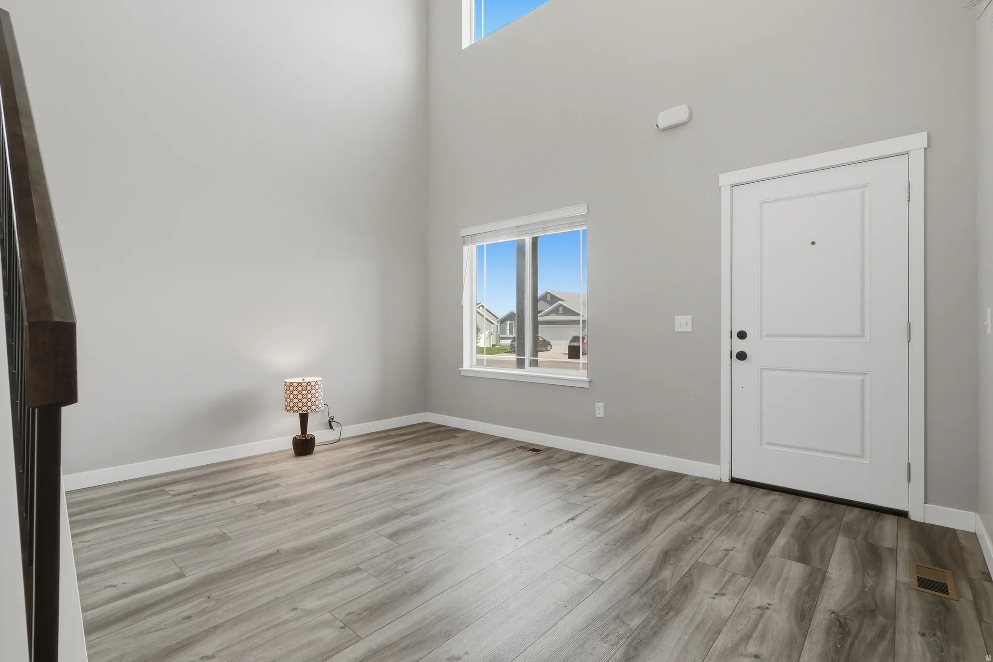 Entryway featuring high ceilings, wood-finish flooring, a contemporary white entry door, and a prominent window