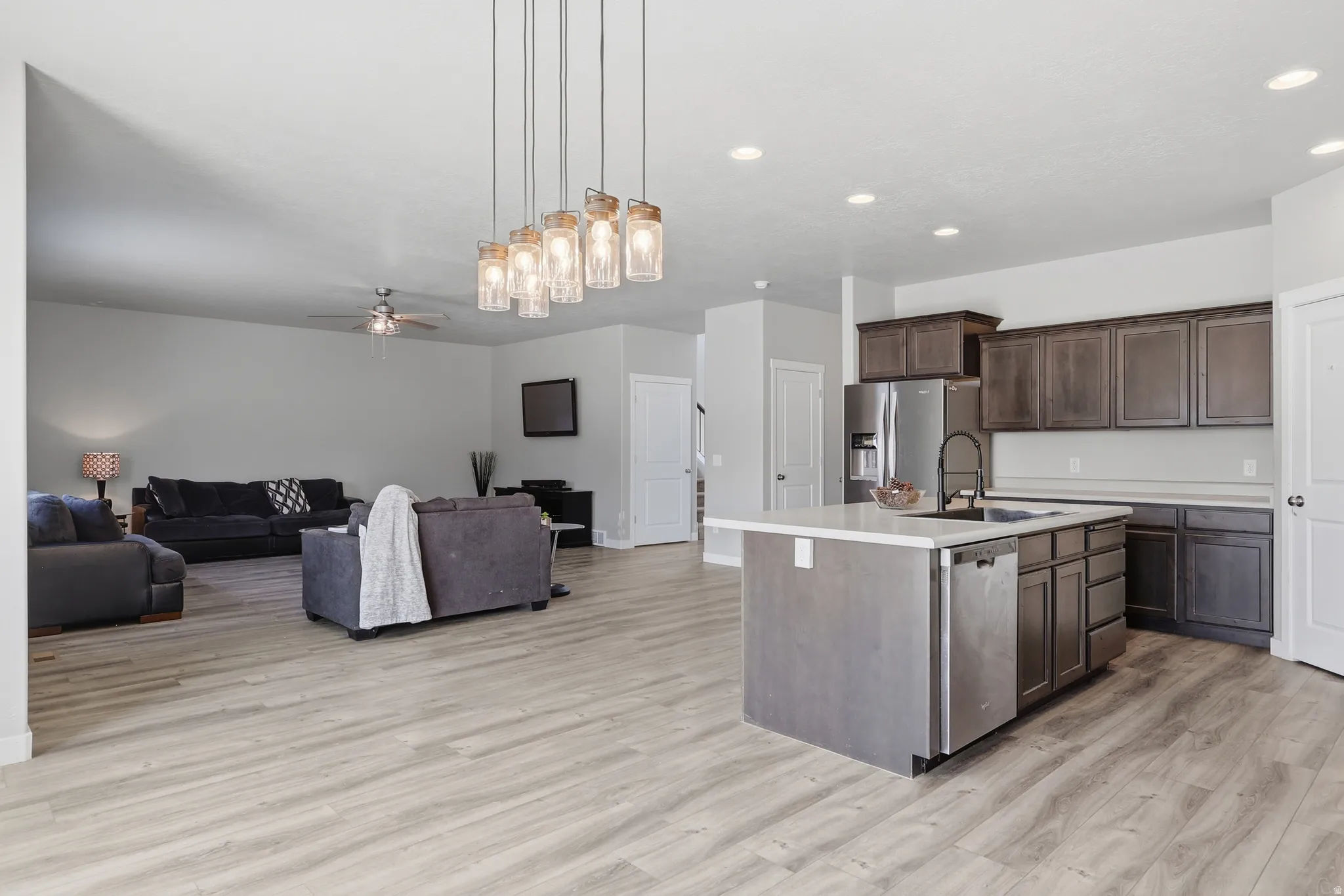 Open-concept living space featuring wood-finish flooring, a kitchen island with light-toned countertop, dark wood cabinetry, and stainless steel appliances