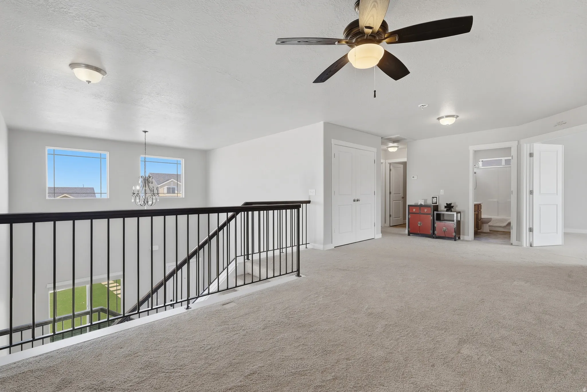 Spacious upstairs landing featuring neutral carpeting, a ceiling fan with integrated lighting, and multiple windows