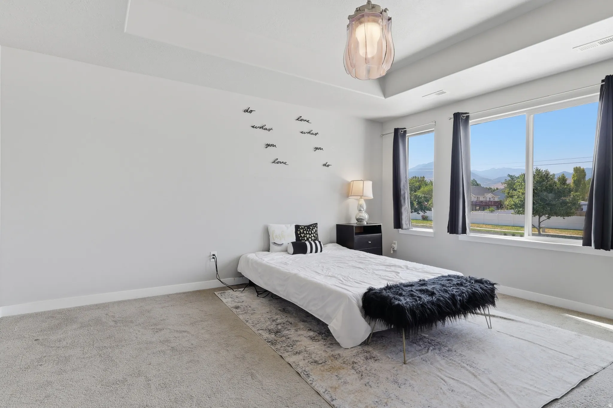 Spacious room featuring a tray ceiling, expansive windows with mountain scenery, a ceiling-mounted light fixture, and light-toned carpeting