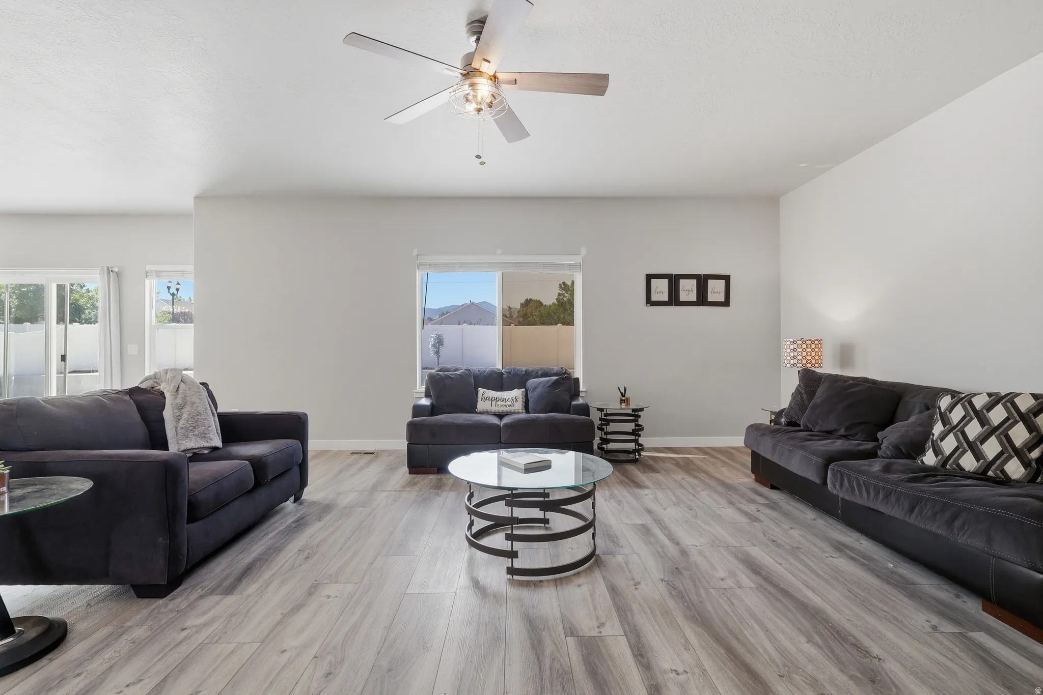 Spacious living area featuring wood-finish flooring and a ceiling fan with integrated lighting