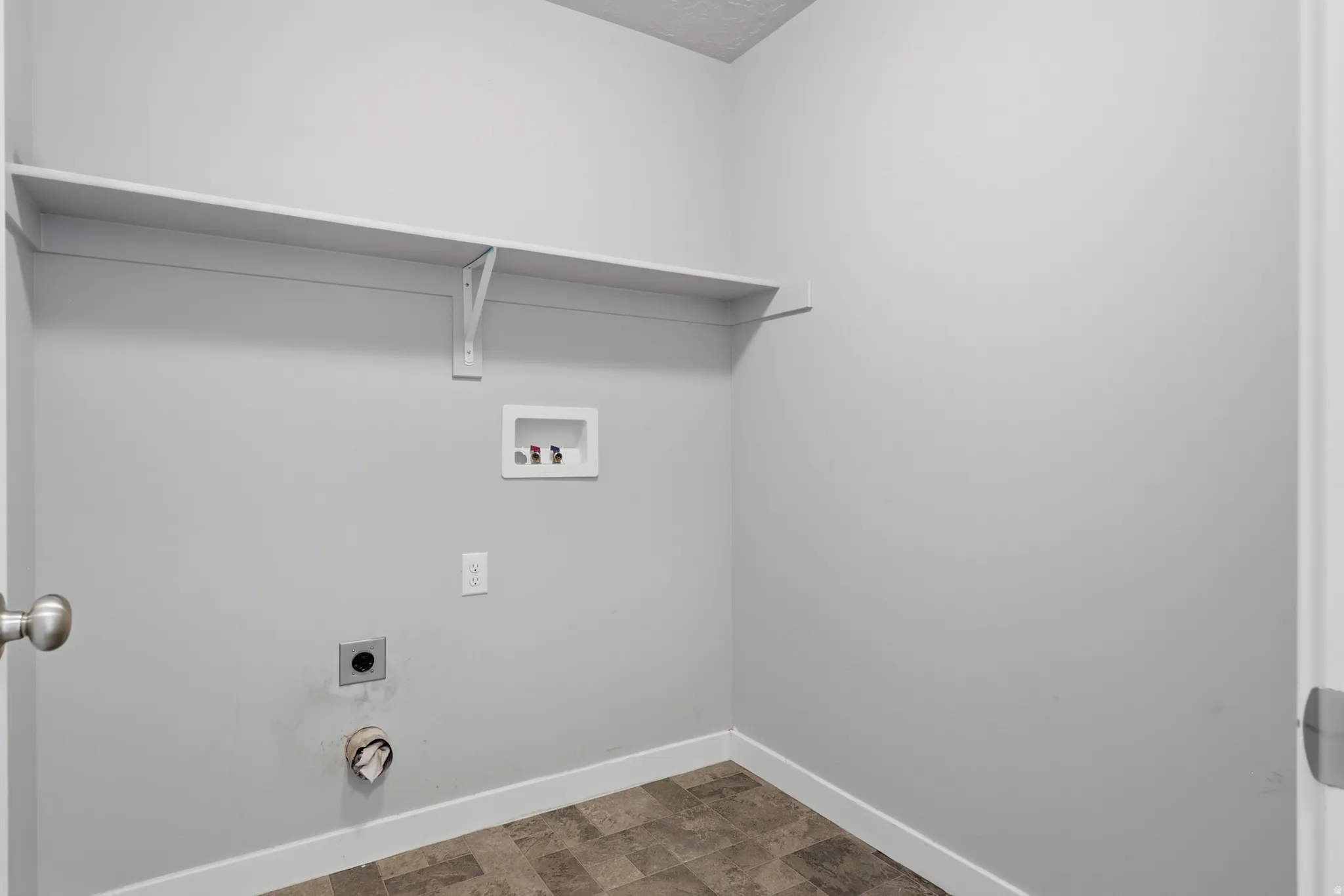 Dedicated utility area featuring a wall-mounted shelf, light gray walls, and durable sheet vinyl flooring