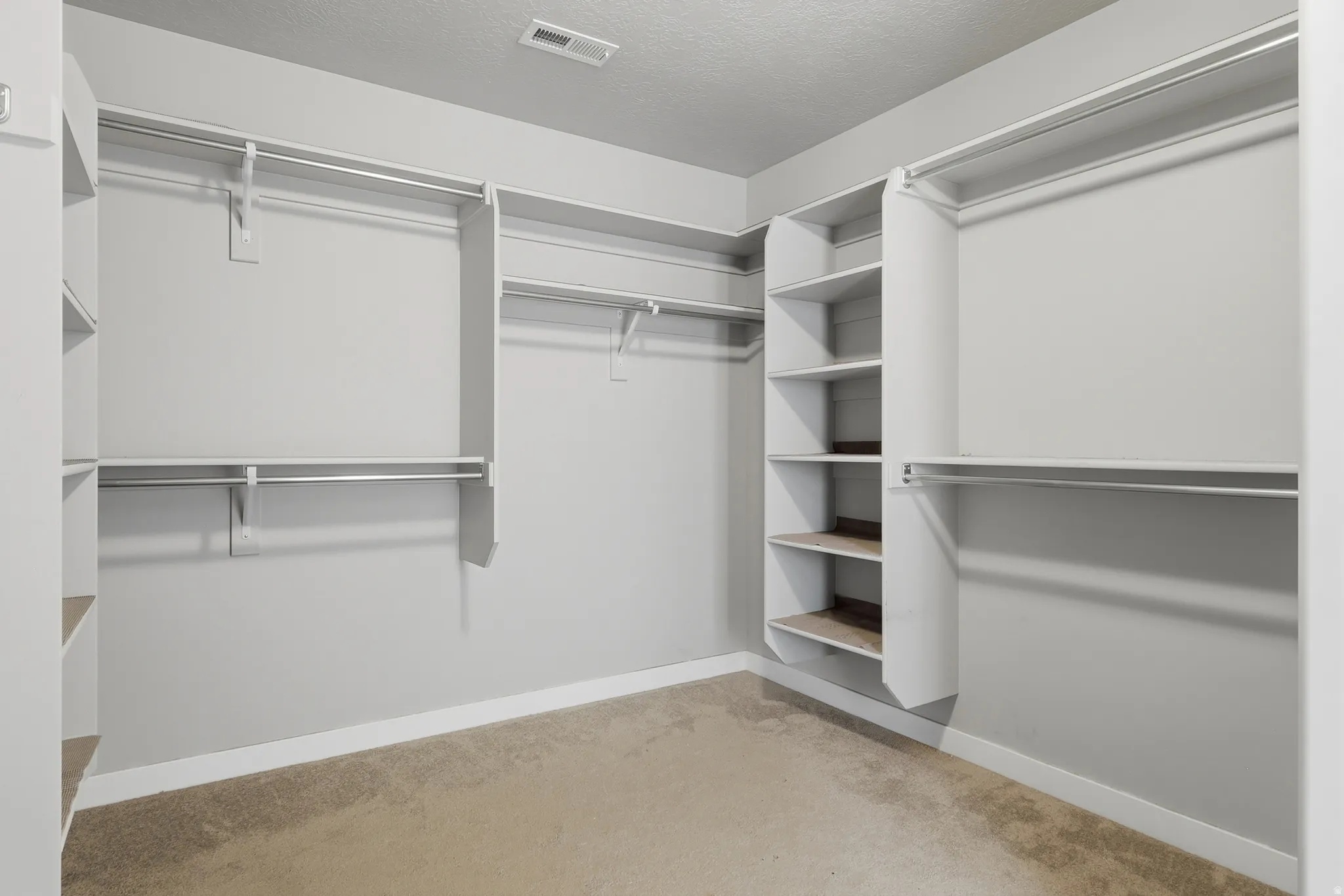 Carpeted closet featuring extensive built-in shelving, multiple hanging rods, white trim, and light gray walls