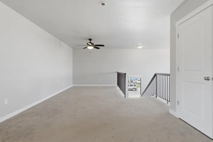 Spacious carpeted upper-level area featuring a ceiling fan, recessed lighting, and a white paneled door