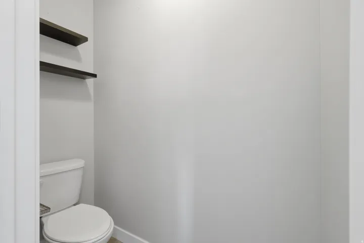 Recessed toilet area featuring a white commode and two dark-finish floating shelves
