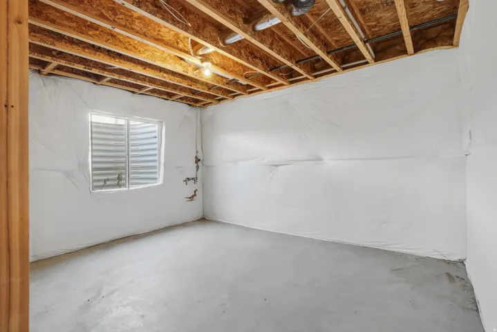 Unfinished basement featuring exposed wood joists, concrete flooring, insulated walls, and a window