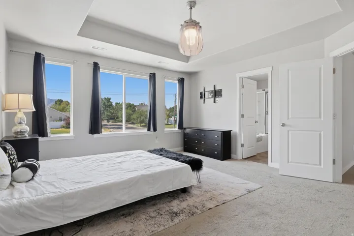 Spacious interior room featuring light gray carpeting, three large windows, a tray ceiling, and a contemporary ceiling fixture