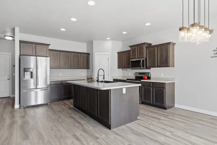 Kitchen featuring wood-finish flooring, dark wood cabinetry, white countertops, a stainless steel refrigerator, and a kitchen island with an integrated sink