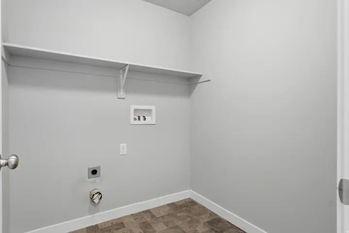 Dedicated utility area featuring a wall-mounted shelf, light gray walls, and durable sheet vinyl flooring
