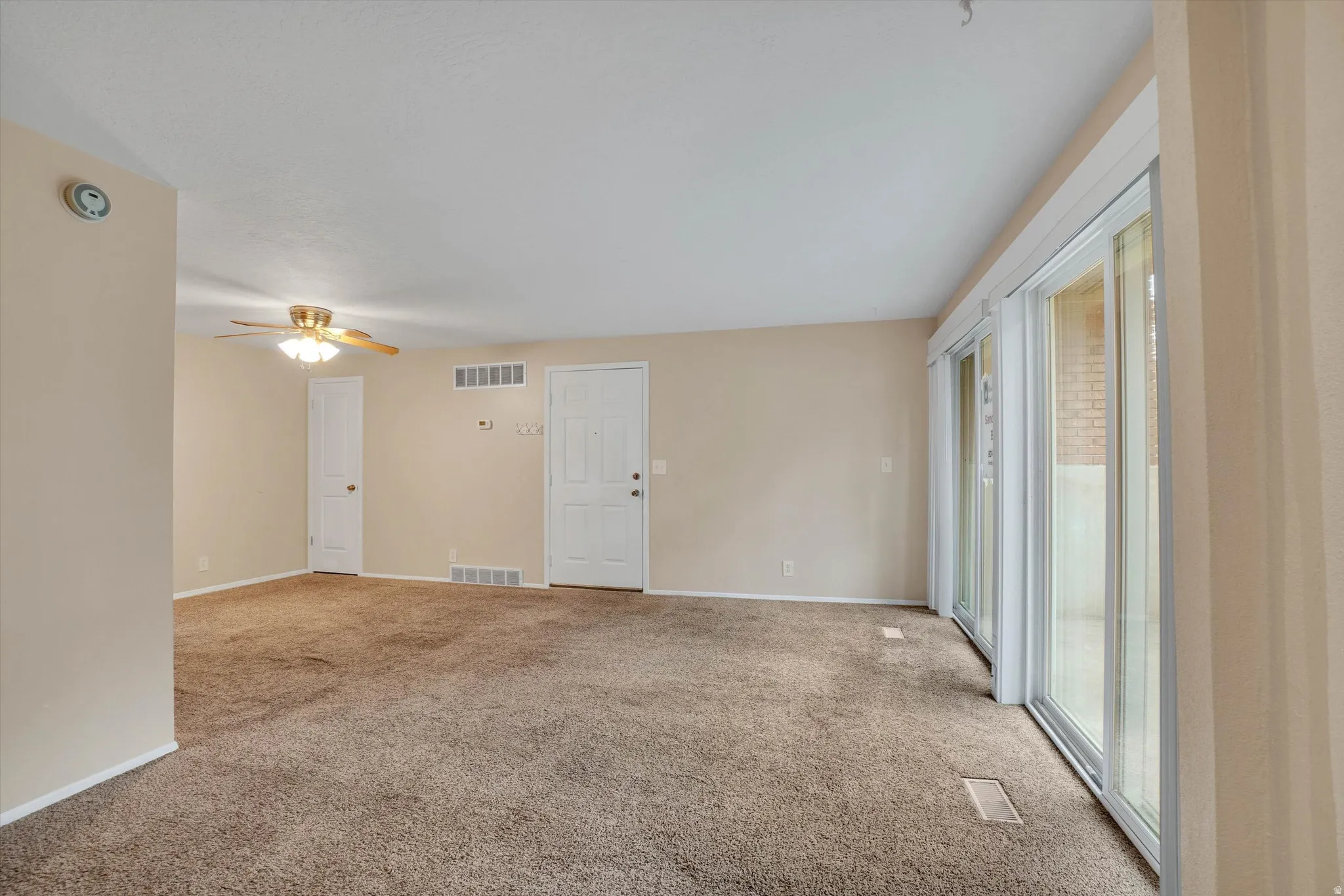 Carpeted flooring throughout, with a ceiling fan light fixture, white interior doors, and sliding glass patio doors