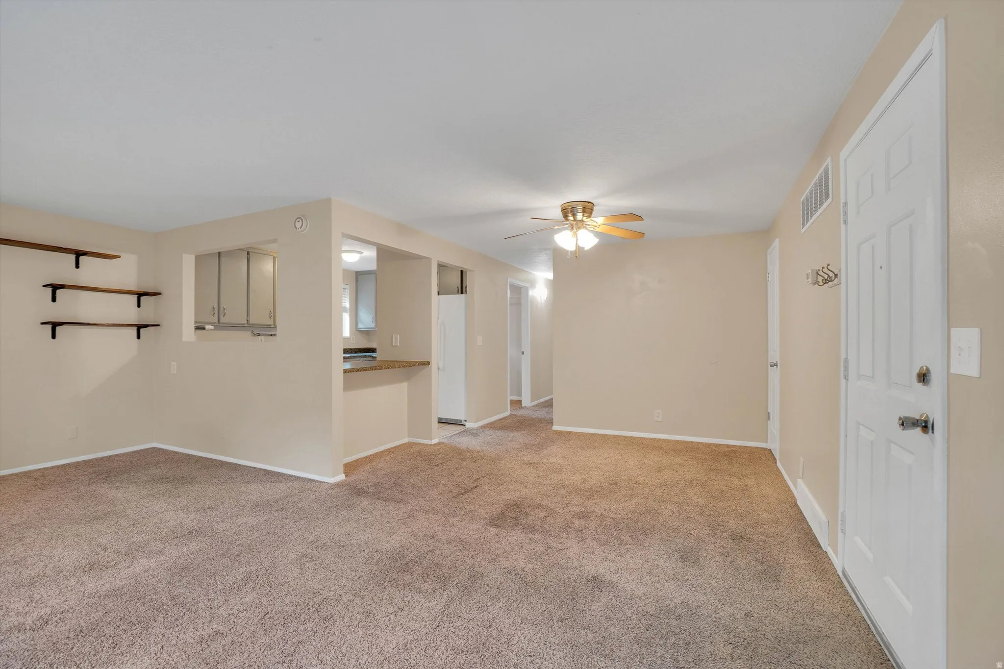 Open-concept living area featuring carpet flooring, ceiling fan, and pass-through counter to the kitchen