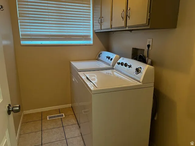 Dedicated laundry space featuring tile flooring, upper cabinetry, and a window with blinds