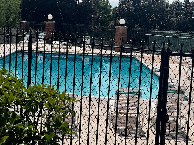Rectangular swimming pool with a surrounding concrete deck, secured by a black metal fence with brick posts