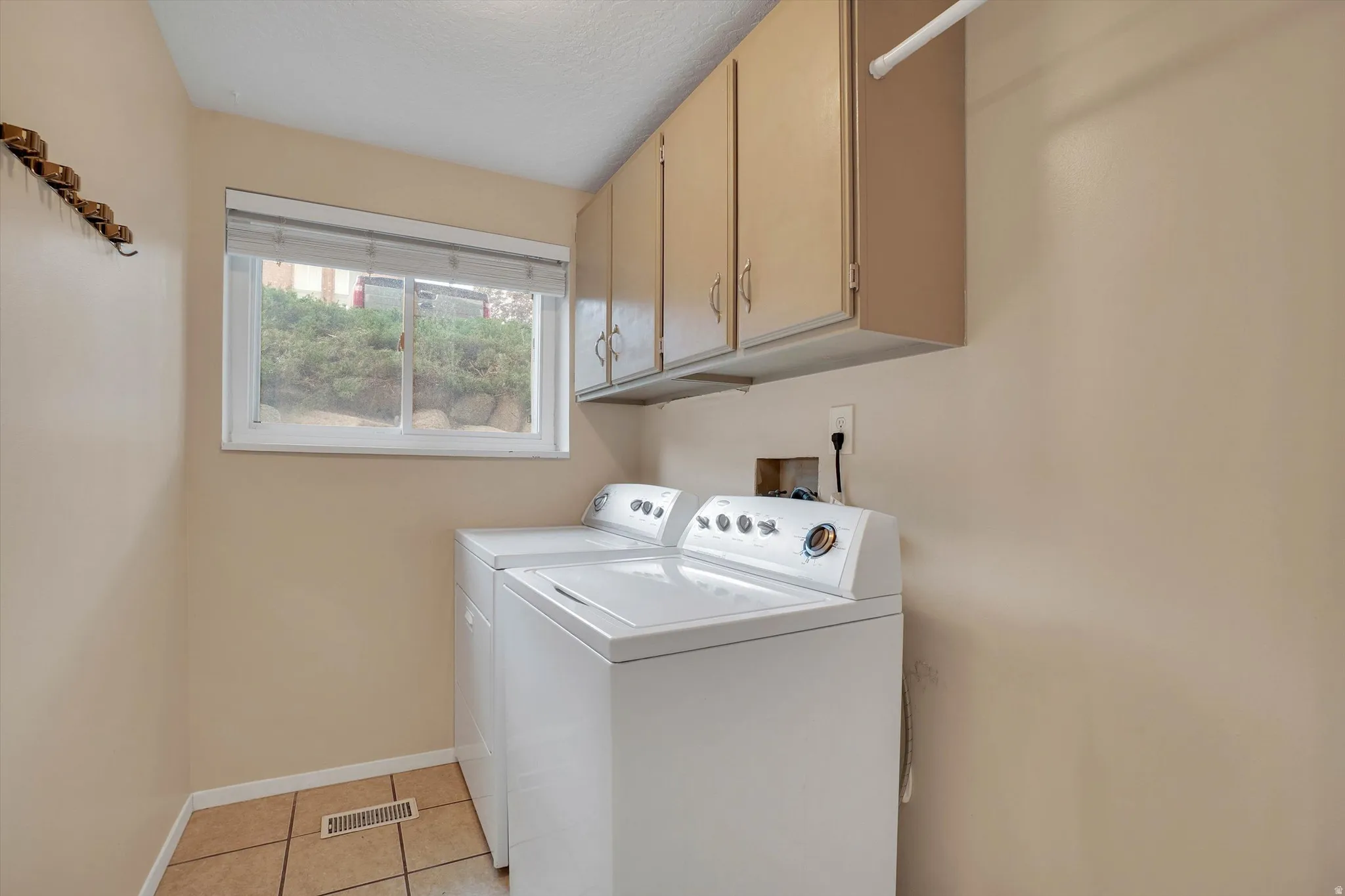 Built-in overhead cabinetry, tiled flooring, window with natural light, and a dedicated clothes hanging rod