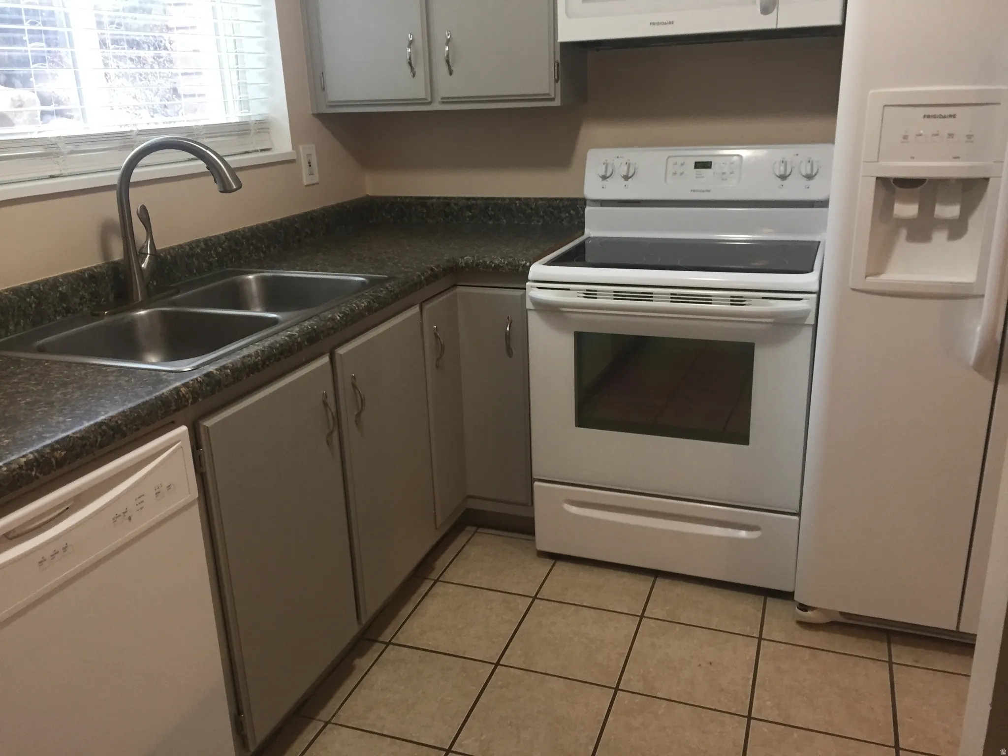 Kitchen featuring white appliances, a double basin stainless steel sink with a gooseneck faucet, light gray cabinetry, and tile flooring