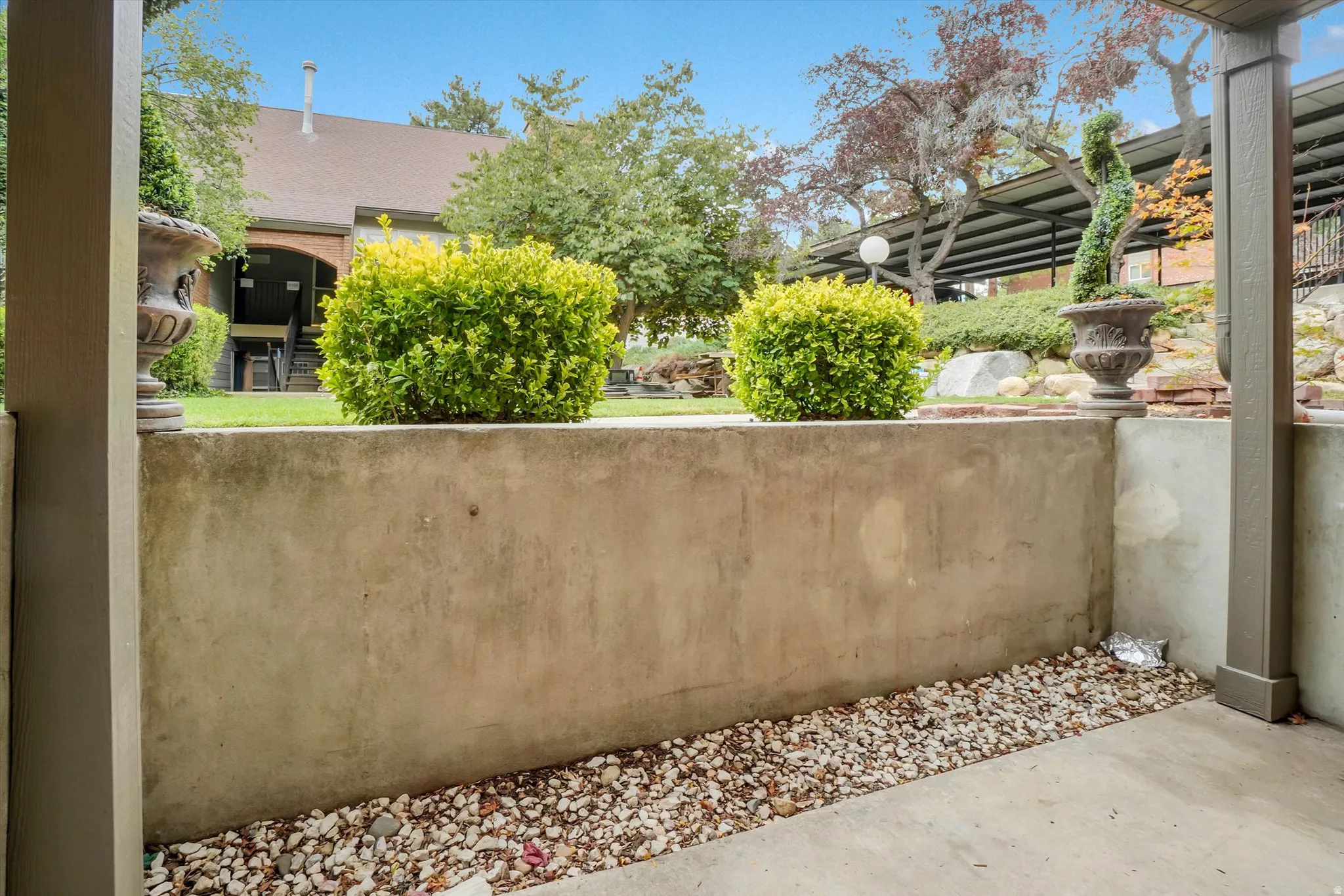 Concrete retaining wall with a gravel bed border, featuring manicured shrubs and decorative urns