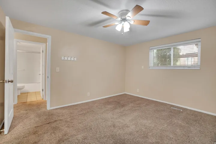 Master bedroom has Neutral tone carpeting, light-colored walls, ceiling fan with integrated lighting, window with blinds, and white interior door