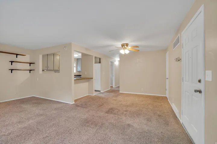 Open-concept living area featuring carpet flooring, ceiling fan, and pass-through counter to the kitchen