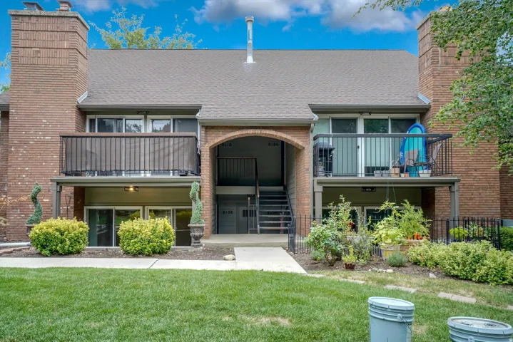 Brick exterior featuring multiple private balconies with black railings, a central arched entryway, and a shingled roof