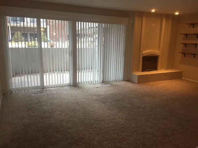 Spacious room featuring broadloom carpeting, a built-in fireplace with hearth, recessed lighting, and a large sliding glass door with vertical blinds opening to a private patio