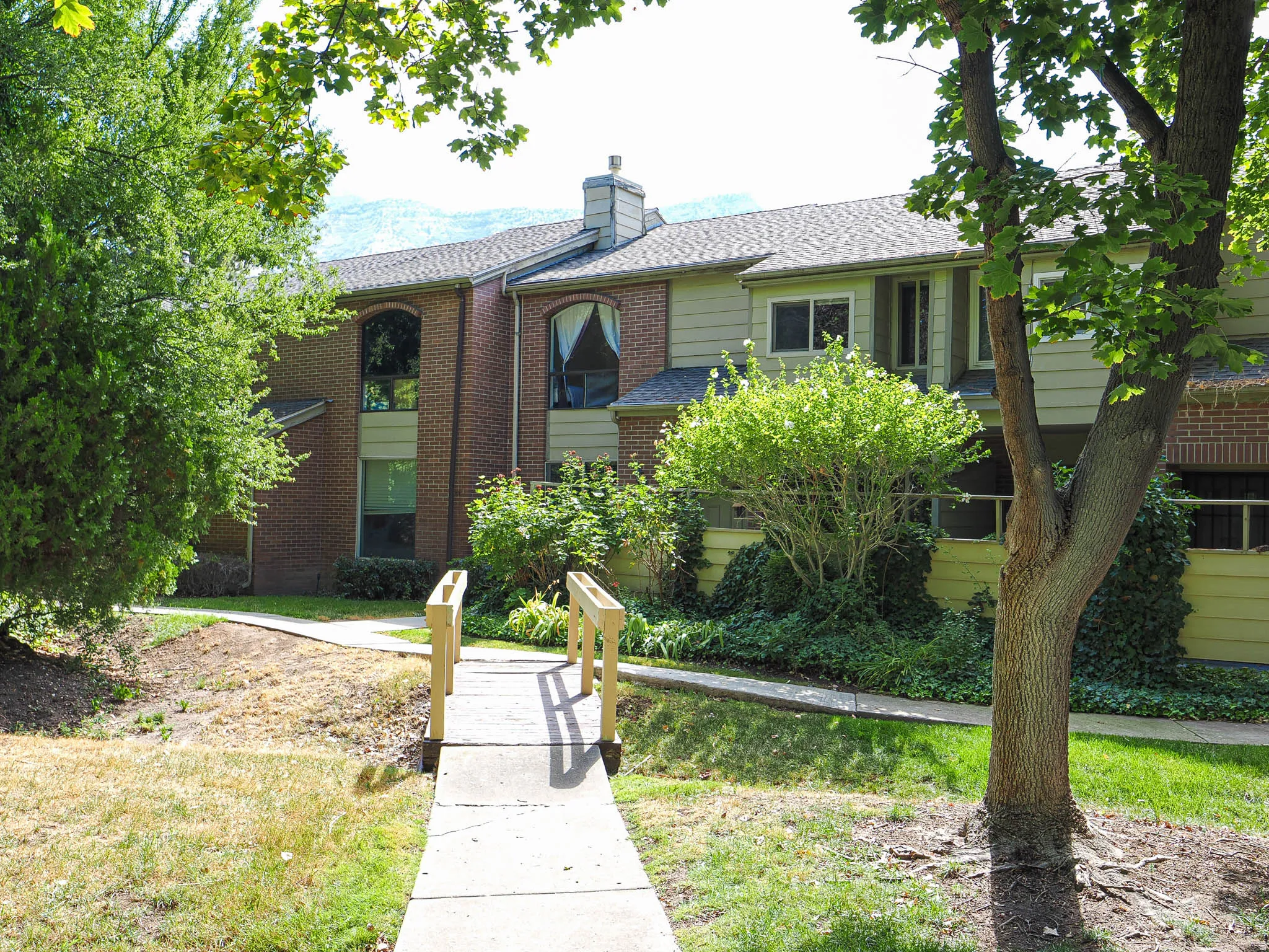 Brick and siding exterior featuring arched windows, a prominent chimney, and mature landscaping