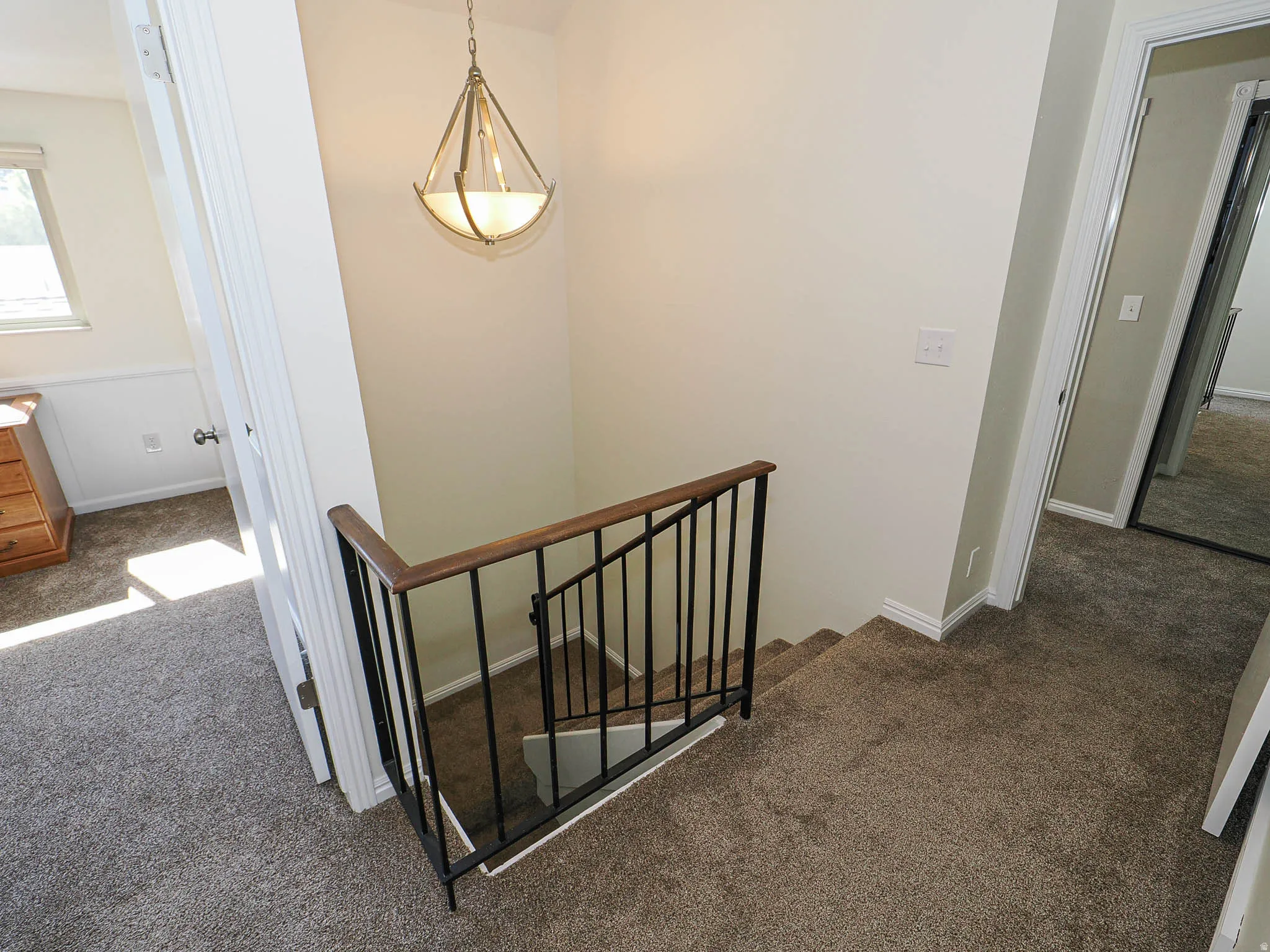 Carpeted landing featuring a wrought iron and wood-finish banister, a decorative hanging light fixture, and a mirrored closet door