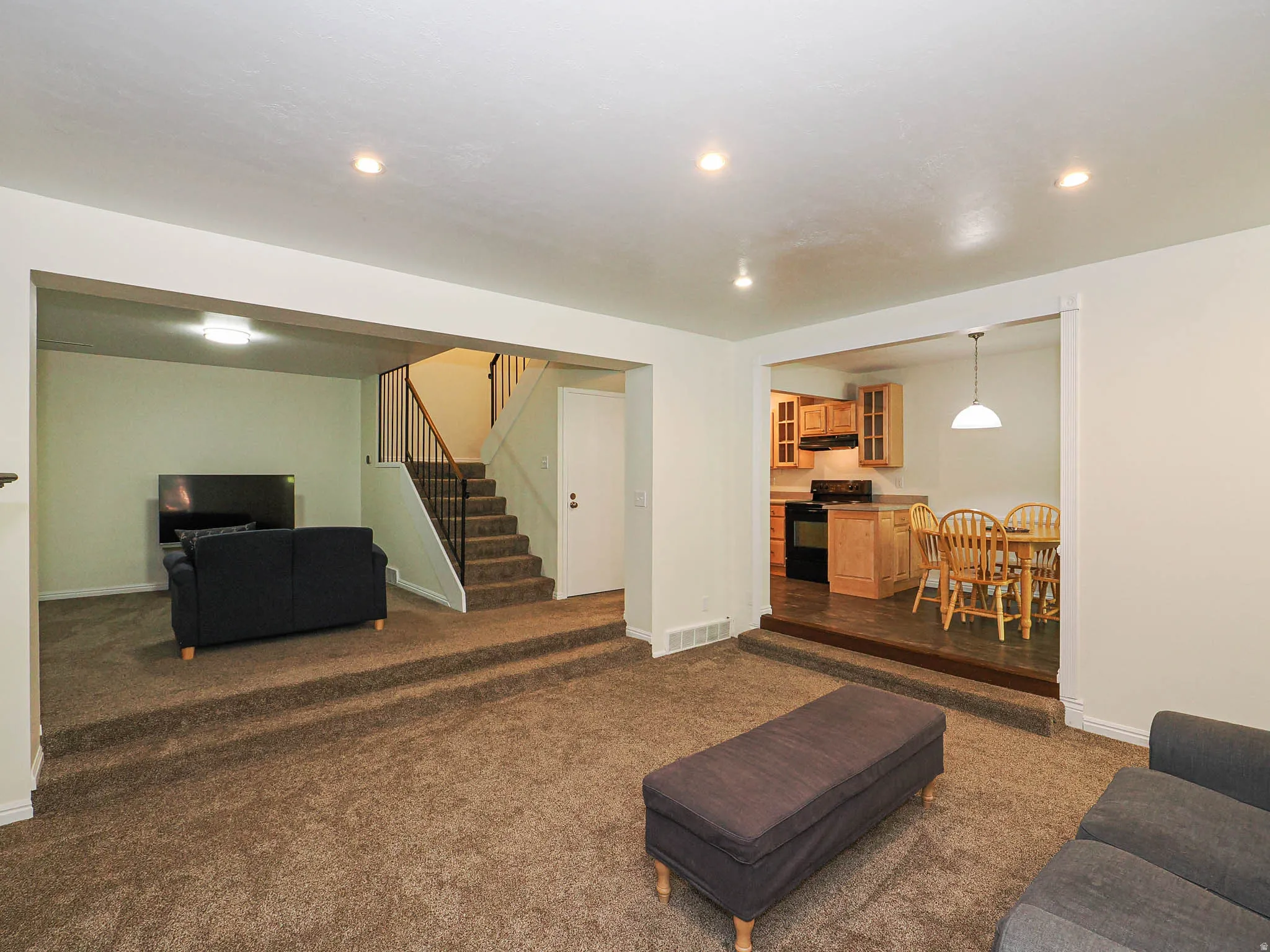 Open-concept living area featuring carpet flooring, recessed lighting, and a stepped transition to a lower-level space