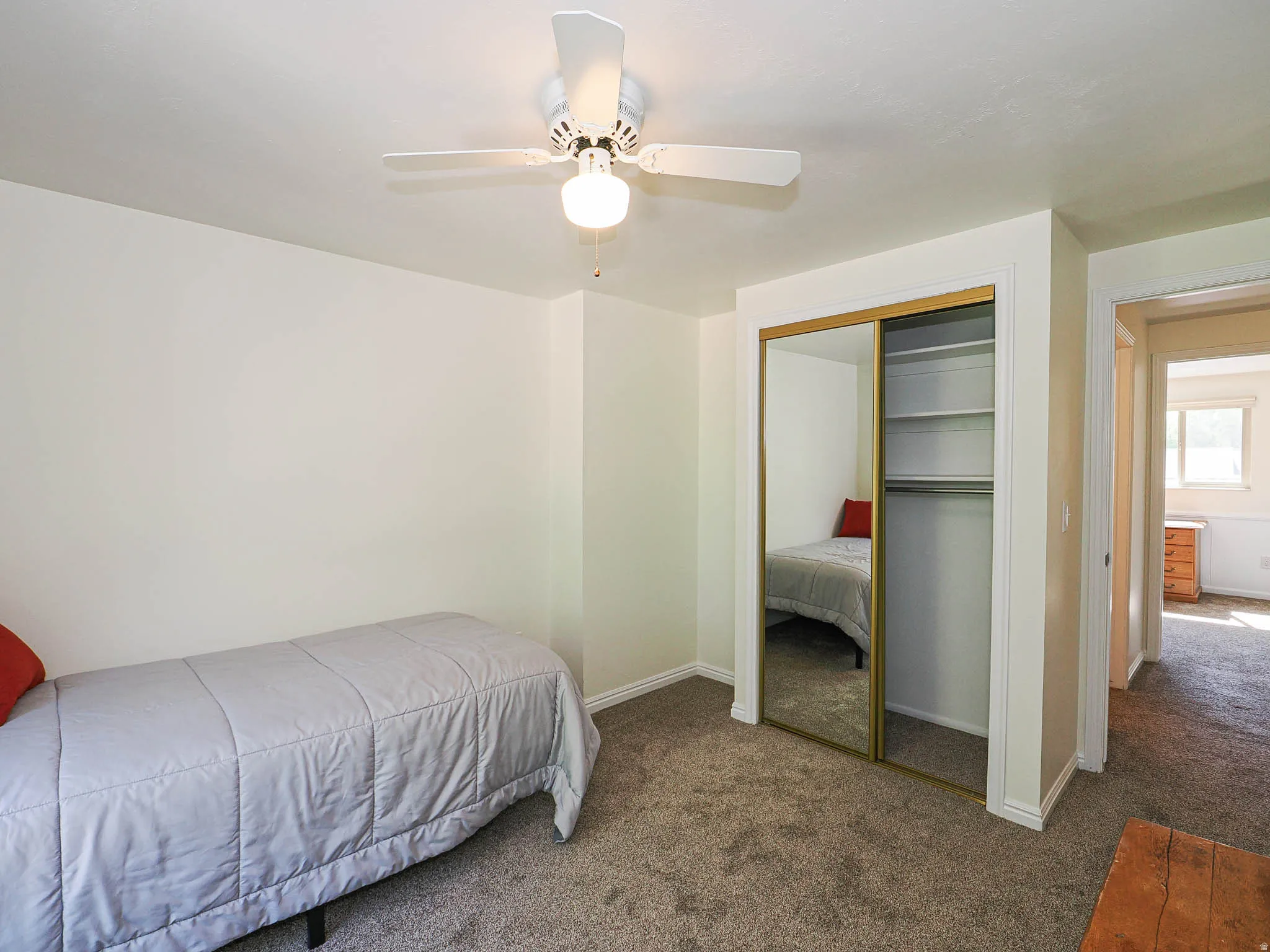 Bedroom featuring ceiling fan with light fixture, mirrored sliding closet doors with shelving, and neutral carpeting