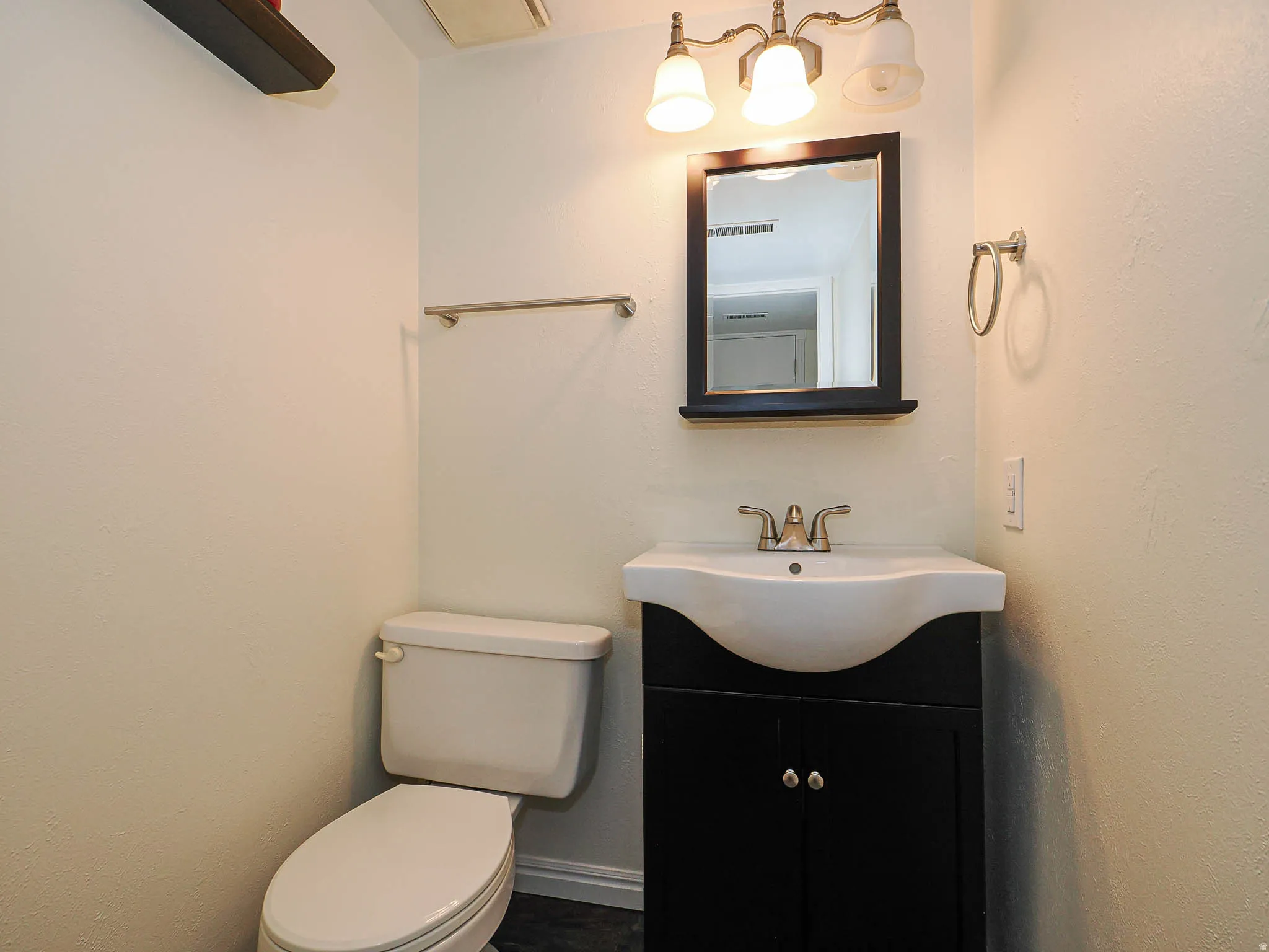 Bathroom featuring a dark wood-finish vanity with a white ceramic sink, brushed nickel faucet, and a rectangular framed mirror with an overhead three-light fixture