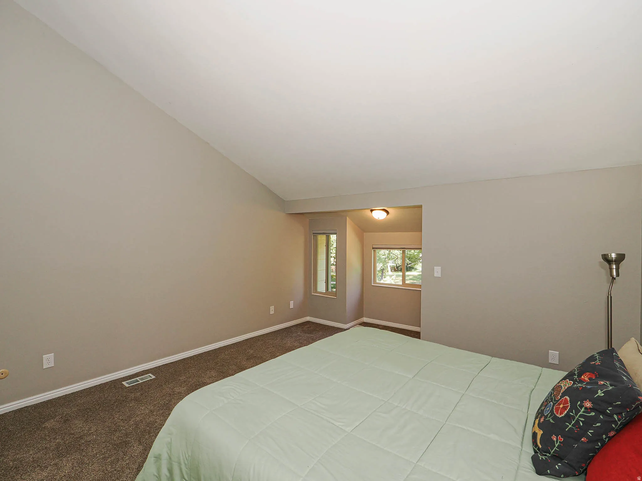 Vaulted ceiling room with neutral paint tones and carpet flooring