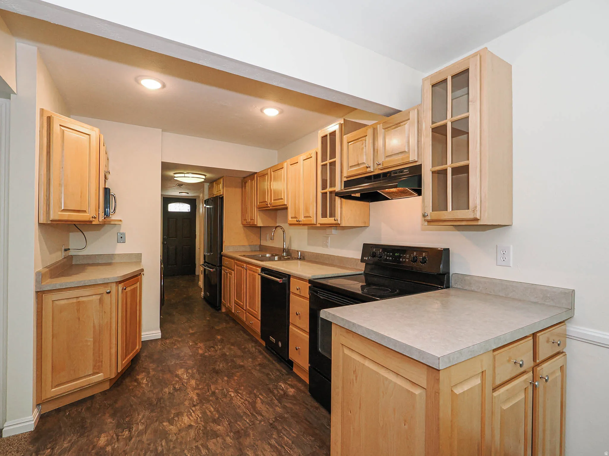 Galley kitchen featuring natural wood cabinetry, laminate countertops, wood-finish flooring, and black appliances