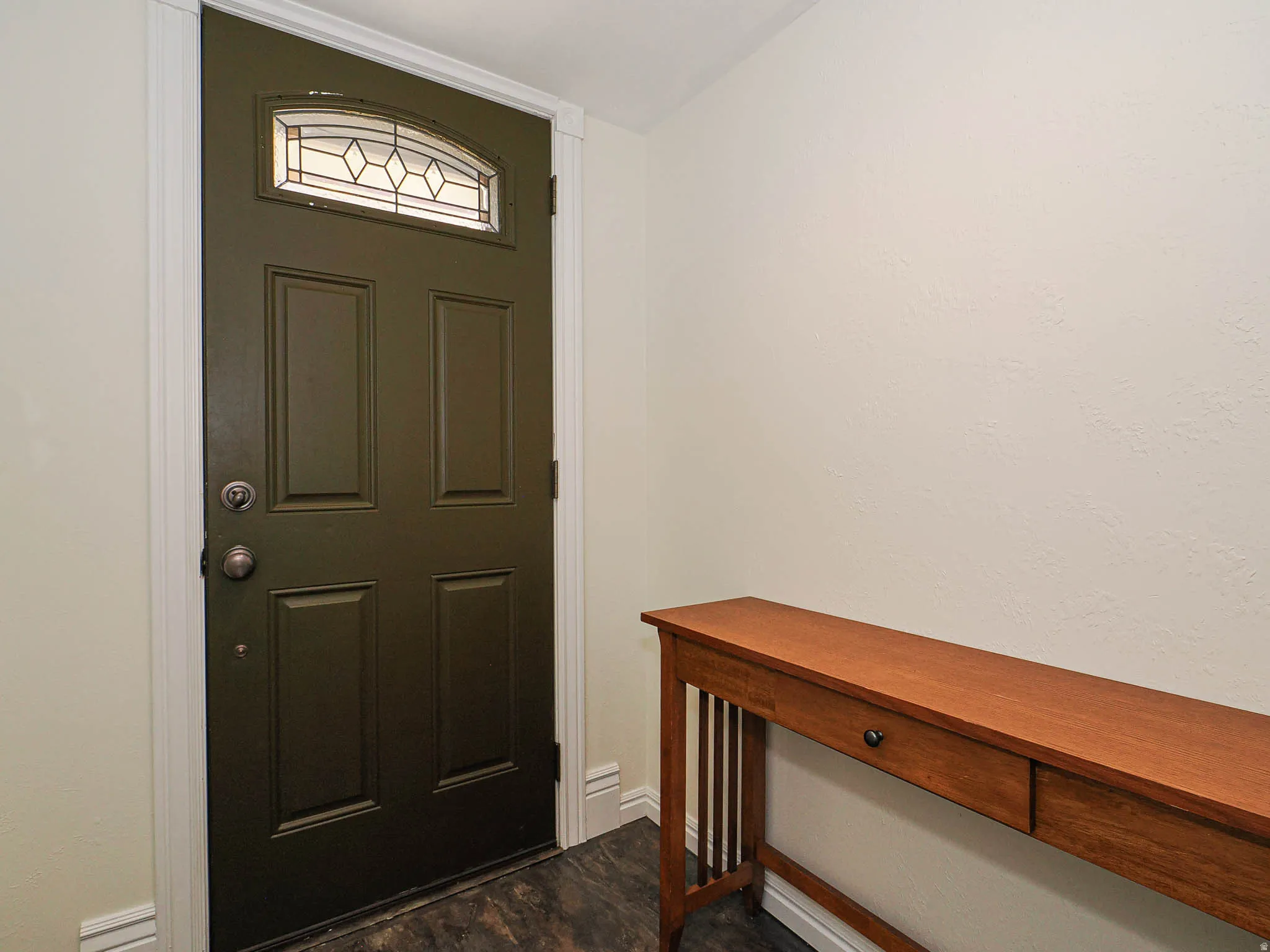 Entryway featuring a dark paneled door with an arched leaded glass transom, white trim, and dark wood-finish flooring