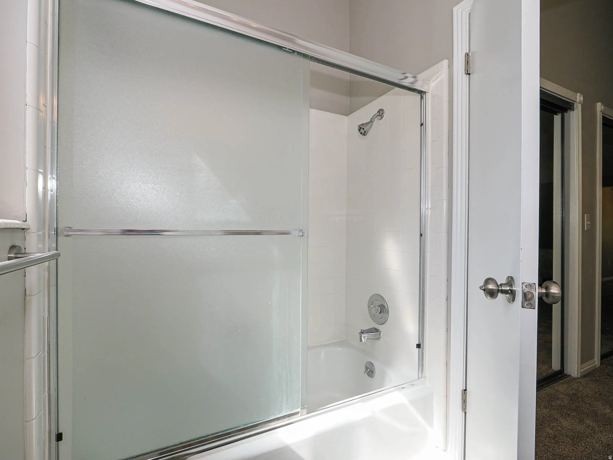 Tub and shower combination featuring a chrome faucet and shower head, white subway tile surround, and sliding frosted glass shower doors
