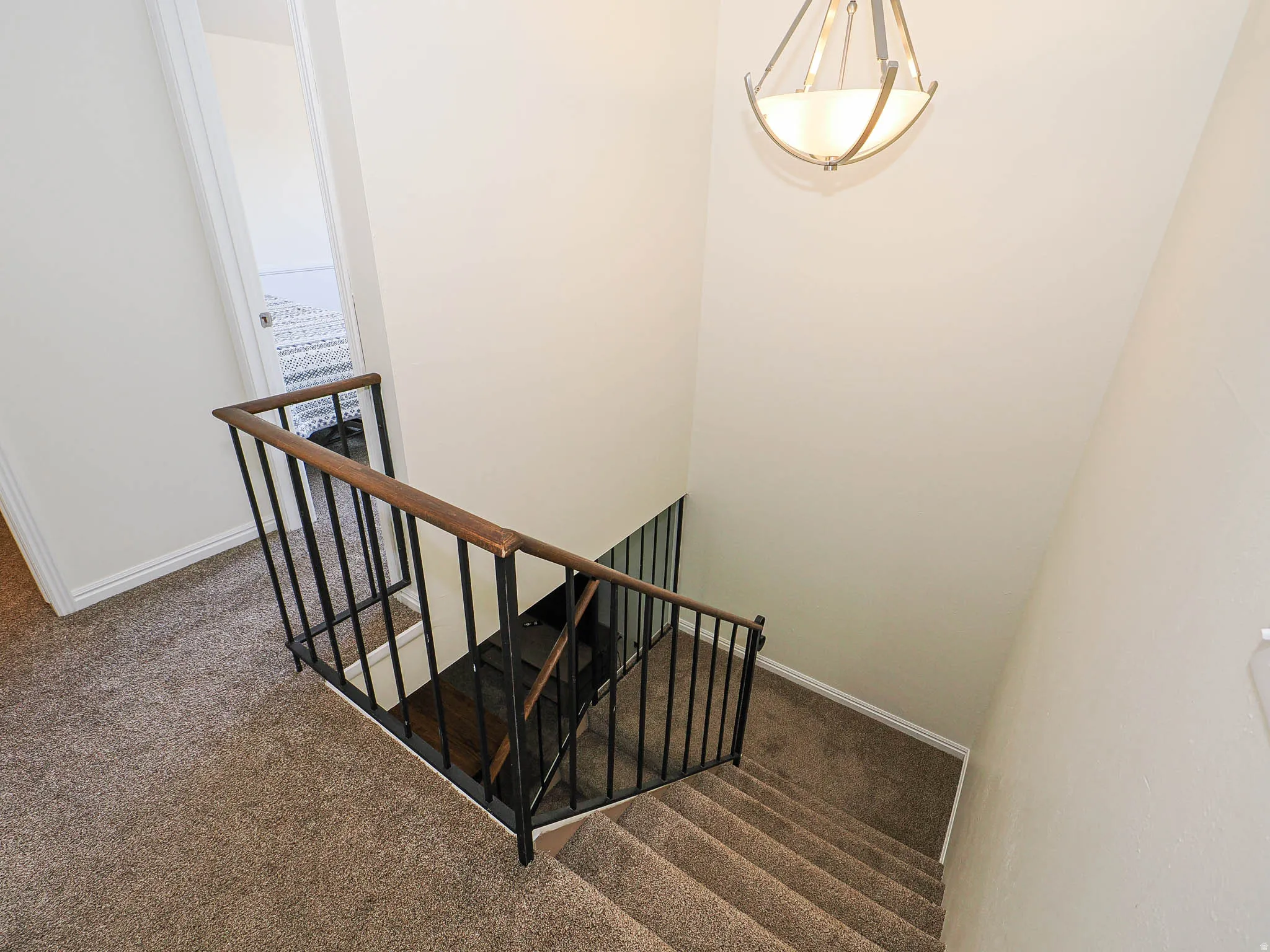 Carpeted staircase with dark metal balusters and a wood-finish handrail