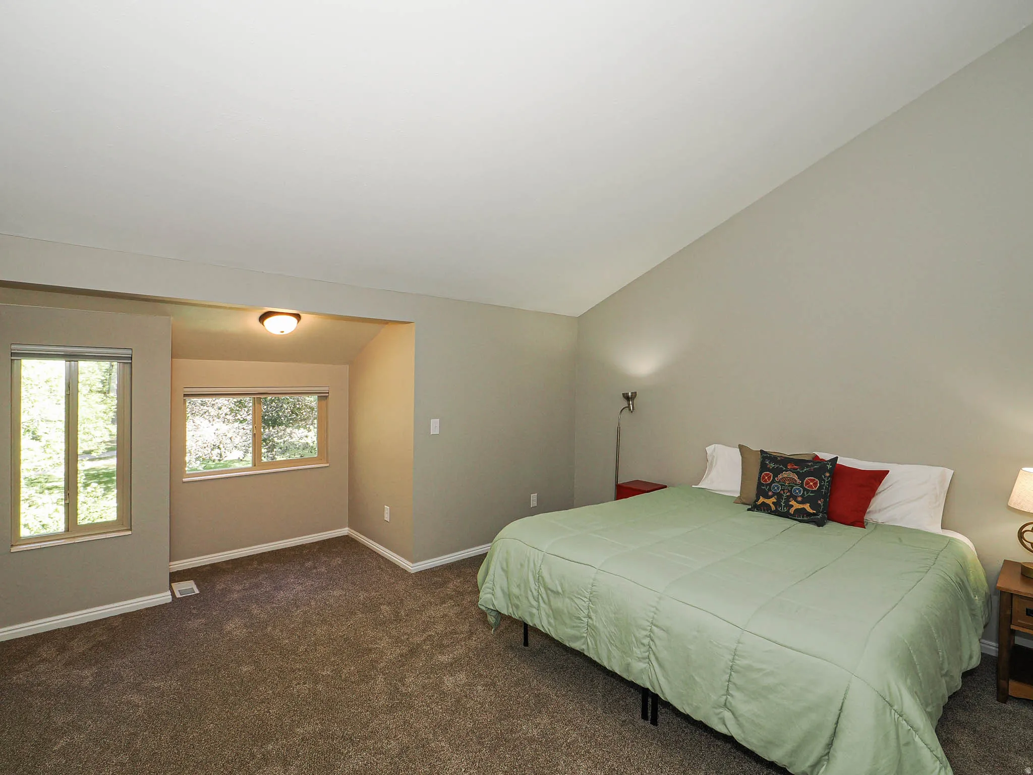 Spacious room featuring vaulted ceilings, plush carpet, and light neutral wall colors