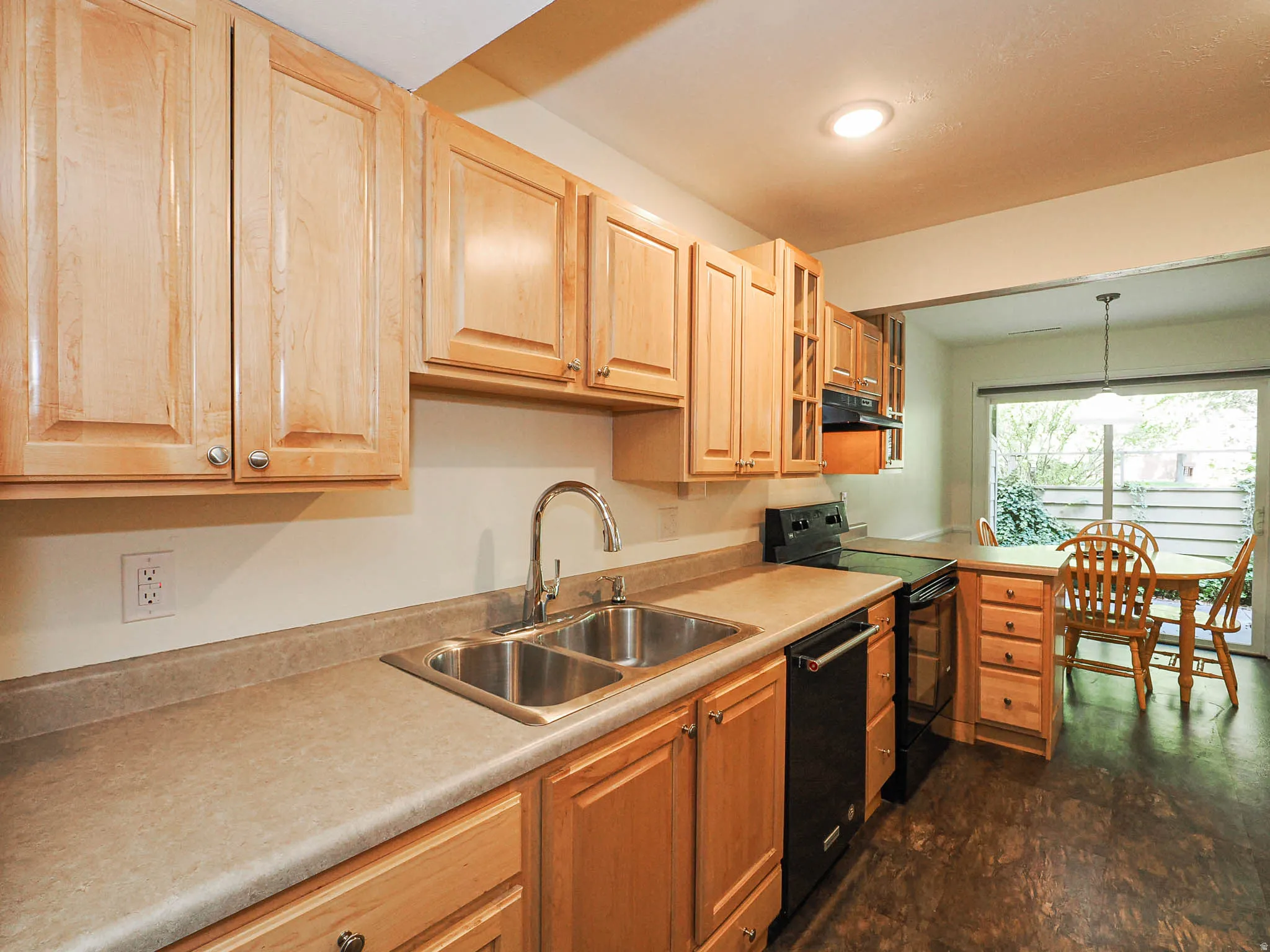Kitchen featuring natural wood cabinetry, light-toned countertops, a stainless steel double-basin sink with a gooseneck faucet, black appliances, and durable flooring