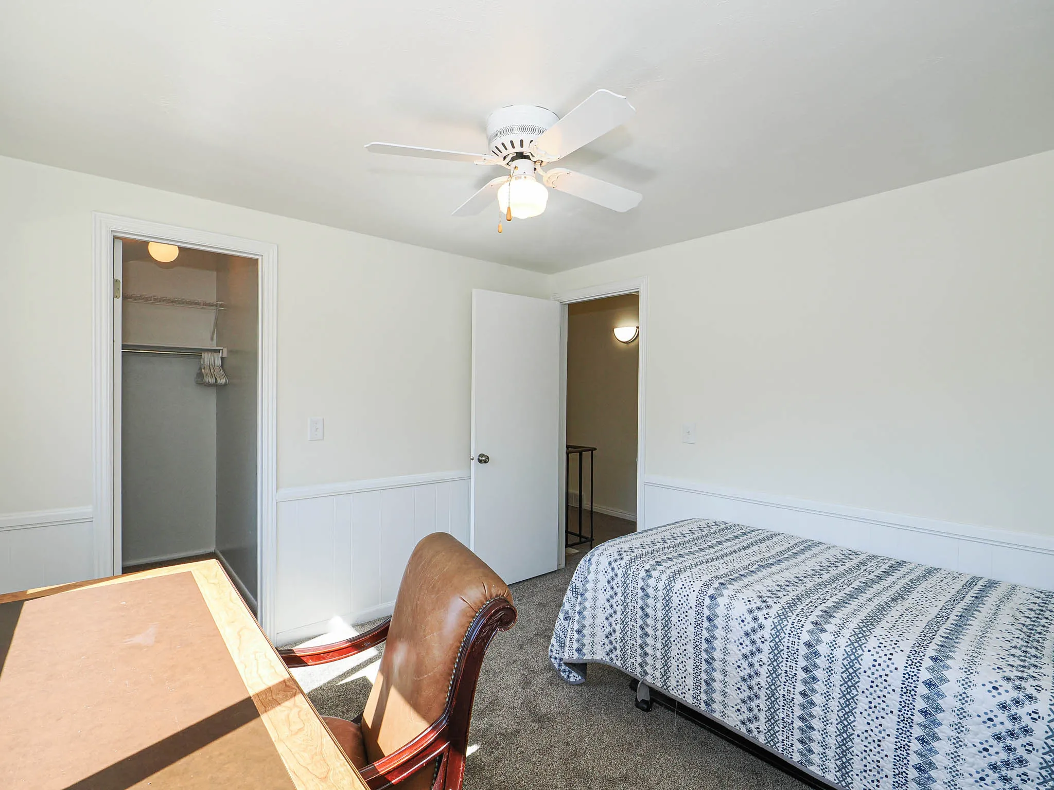 Carpeted room with a ceiling fan, white wall paneling, and a closet featuring a built-in shelf and hanging rod