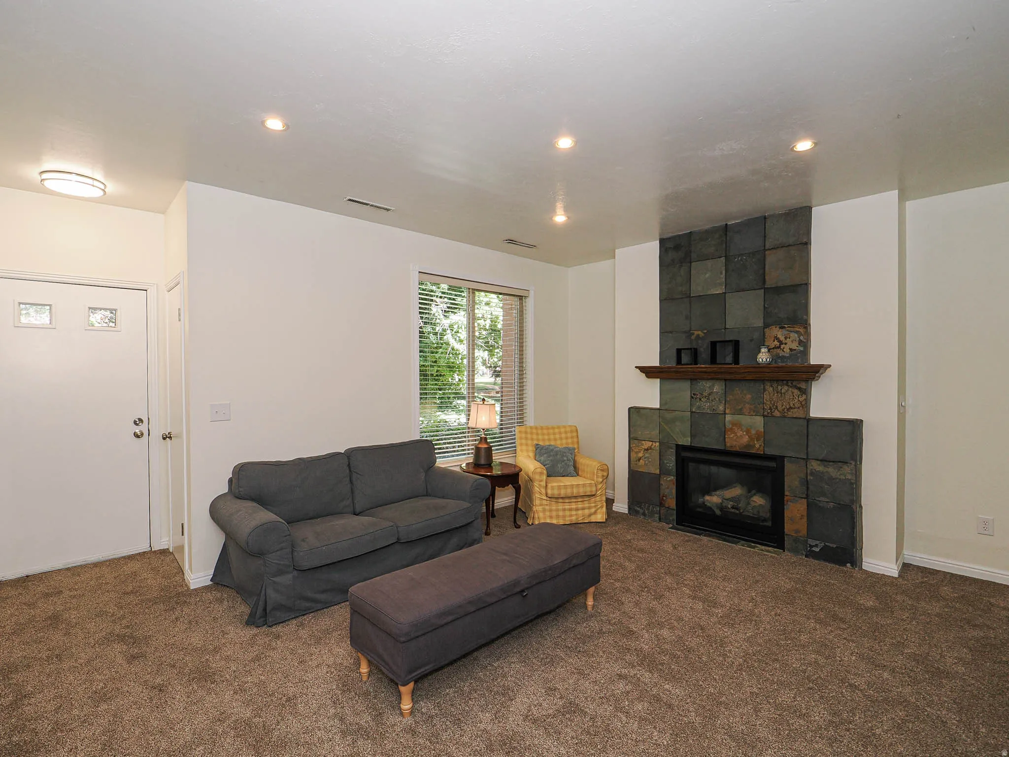 Living area featuring a floor-to-ceiling slate-tiled fireplace with a wood mantel, recessed lighting, and a window with blinds